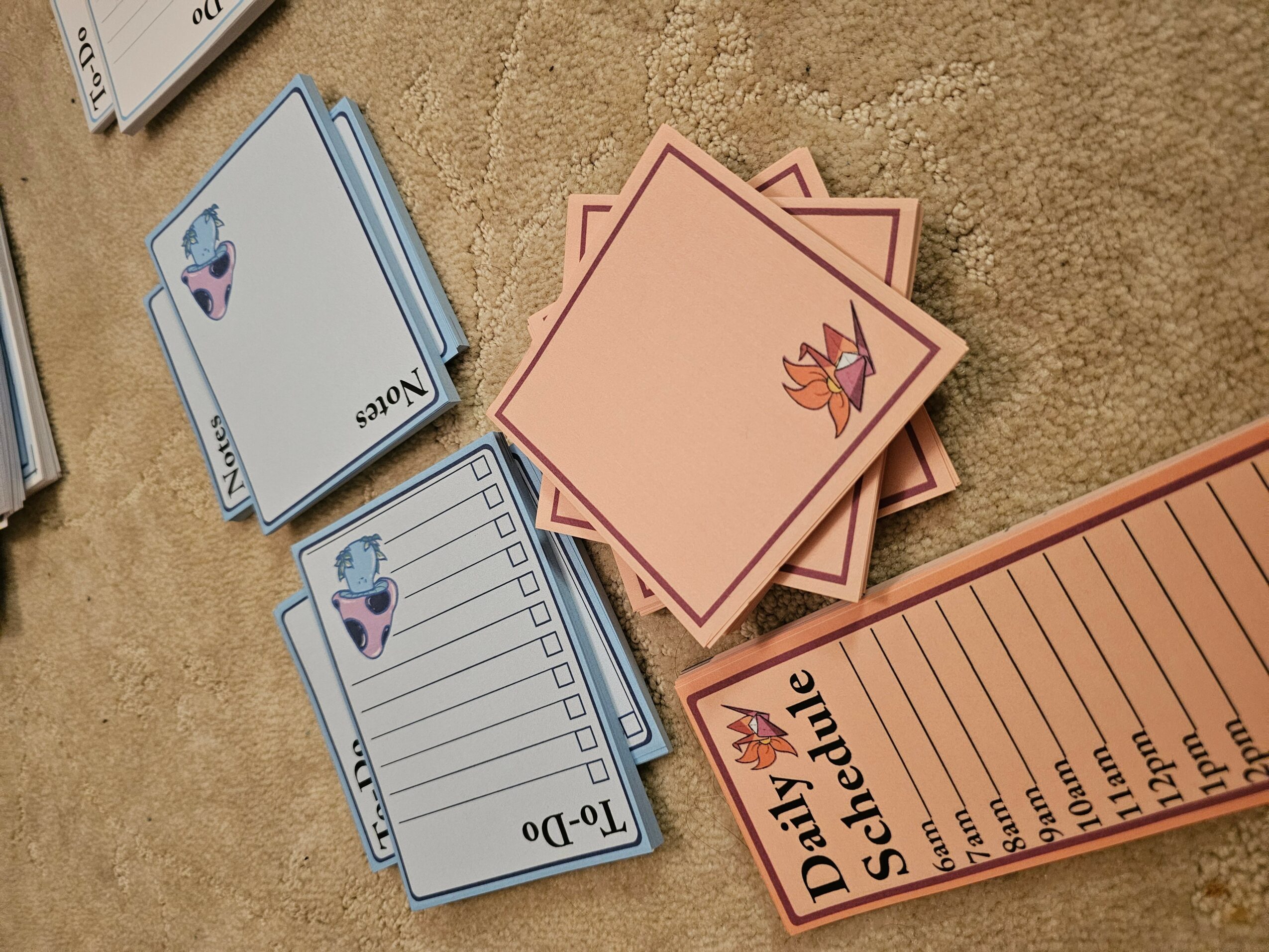 Stack of pink cards with a fox illustration, a blue and white daily schedule, and a lined notepad on a beige surface.
