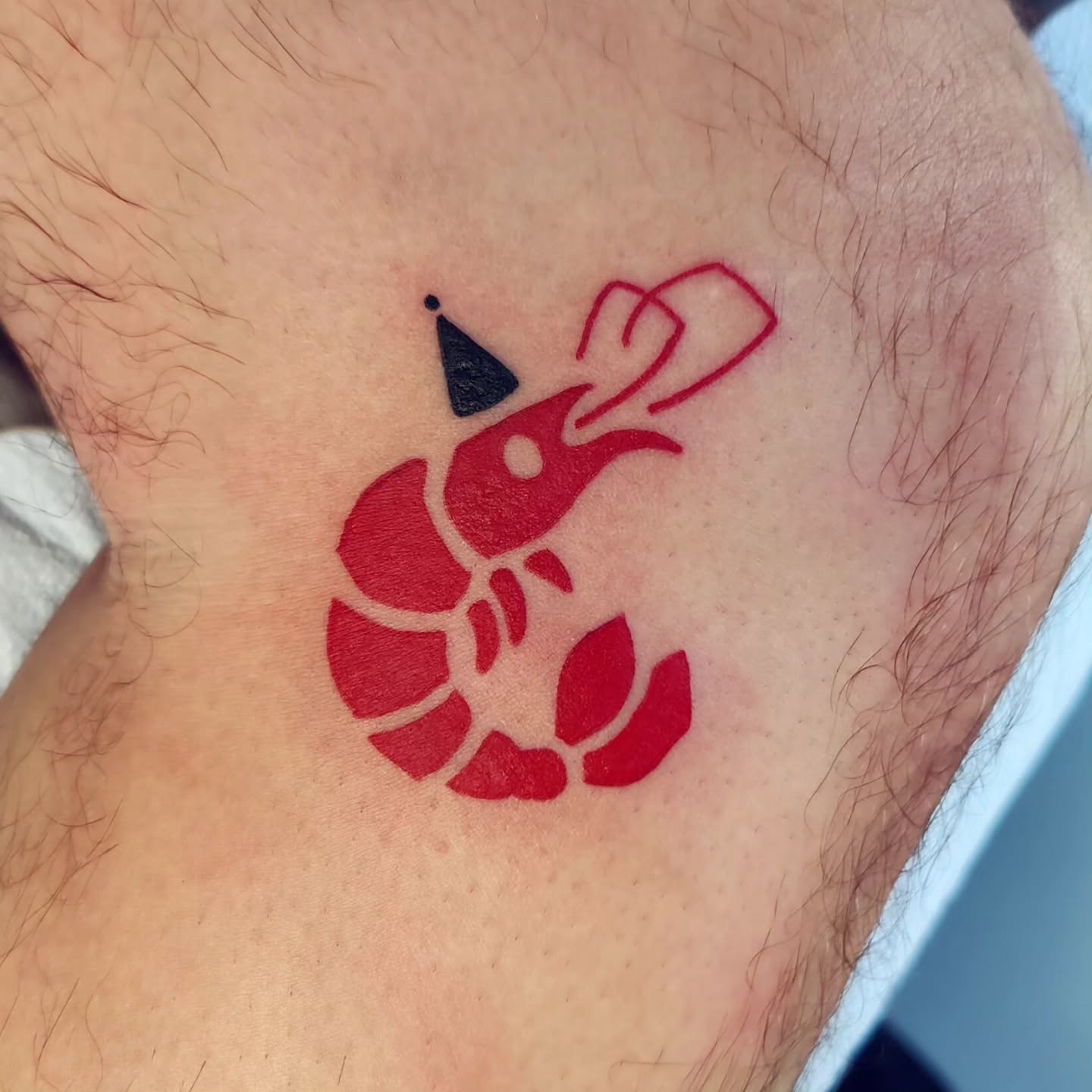 Red lobster tattoo with a black party hat on a person's skin.