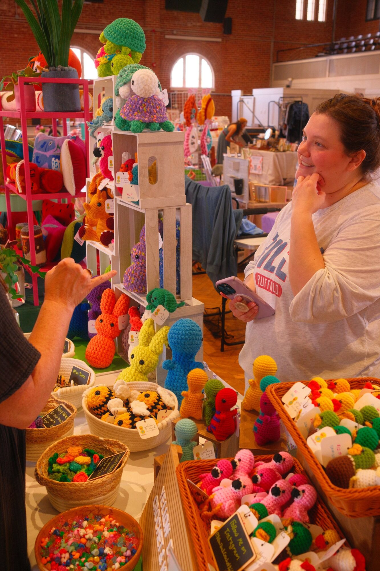 Person browsing colorful handmade crafts and decorations at an indoor market or craft fair.