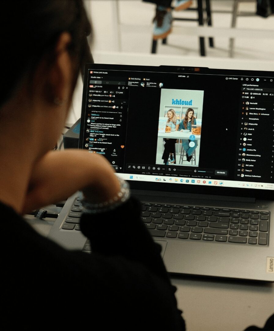 Person working on a laptop with a design software open, showing a magazine cover with two women, in a room with chairs.