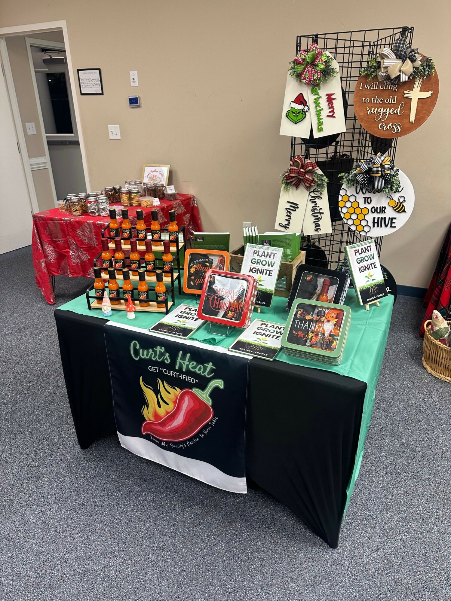 Display table with holiday-themed items, cards, and a cloth with a chili pepper logo, set against a beige wall.