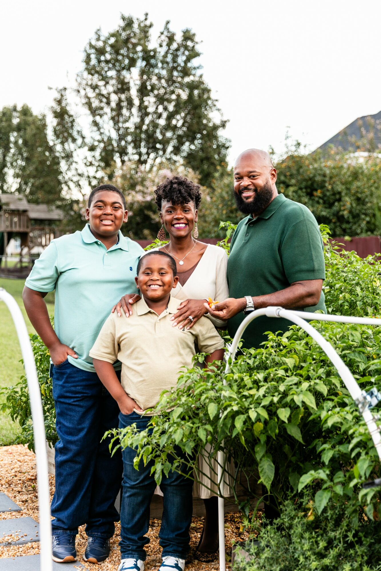 Four people standing outdoors near plants, smiling, with trees and a mountain in the background.