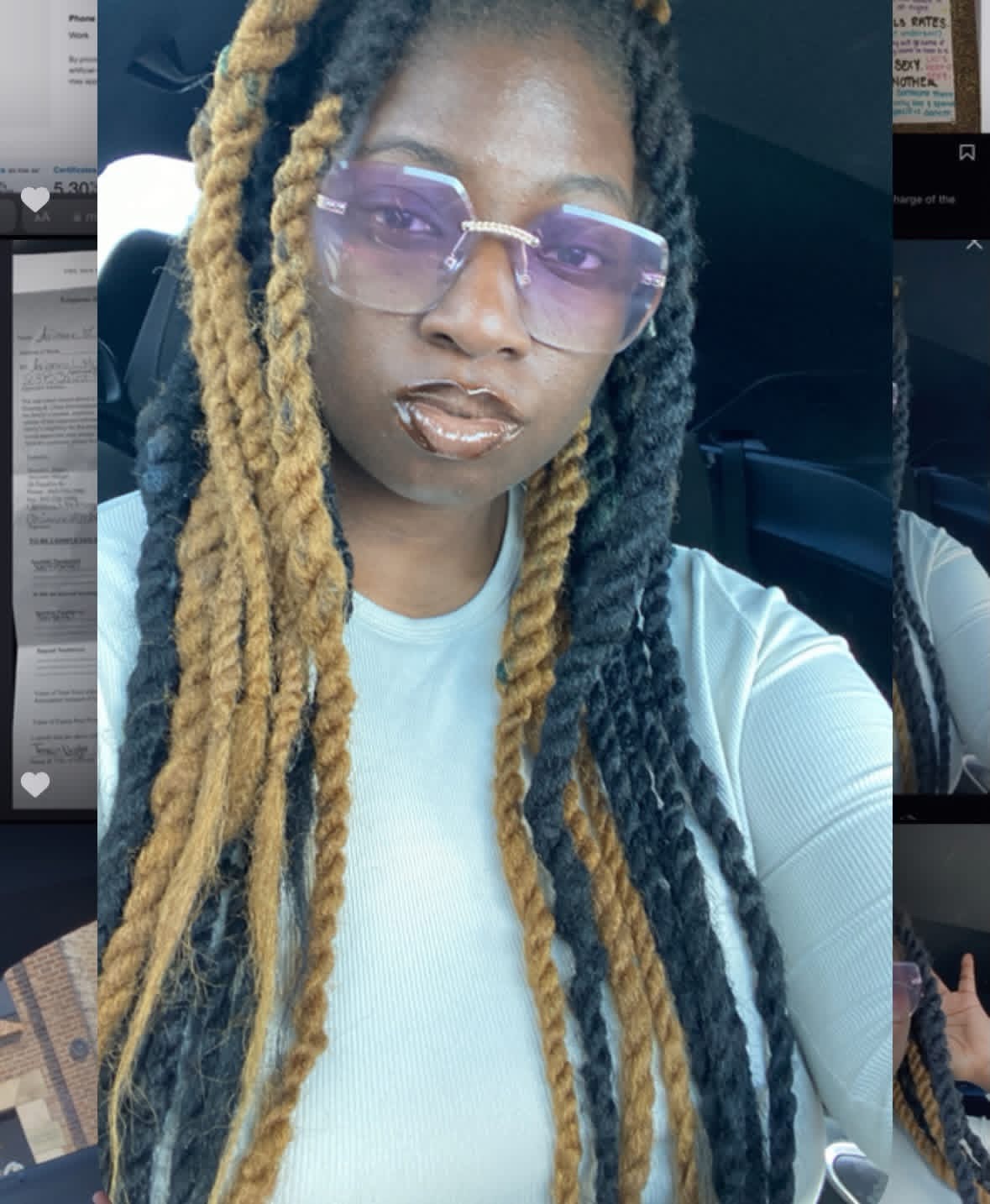 Woman with long blonde and black dreadlocks wearing purple sunglasses and a white top, sitting in a car.