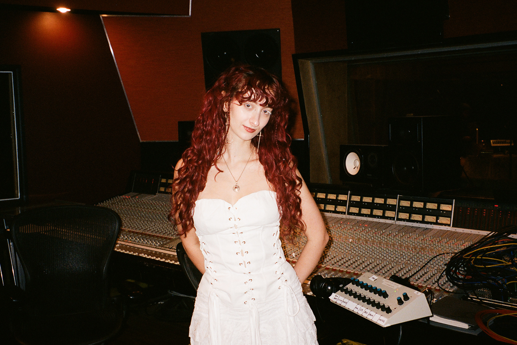 Woman with long curly hair in a white dress standing in a recording studio with equipment