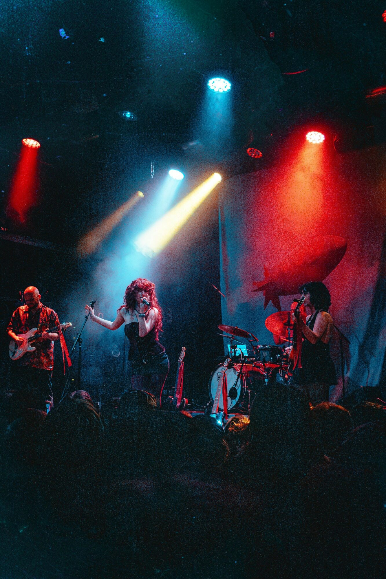 Band performs on stage with colorful lights, including red, blue, and yellow, illuminating the musicians and instruments.