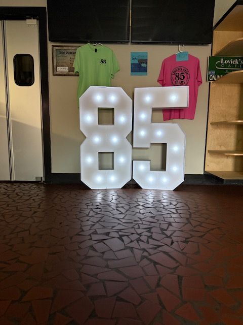 Illuminated number 86 with colorful clothing items on display behind it, on a textured floor.