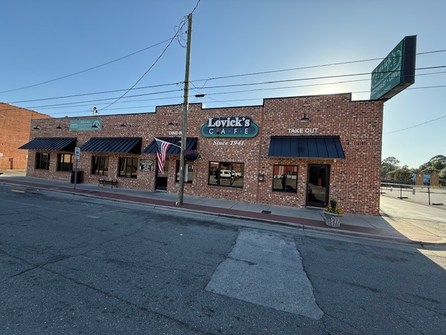 Brick building with signs, awnings, and American flags on a street corner, under a clear sky.