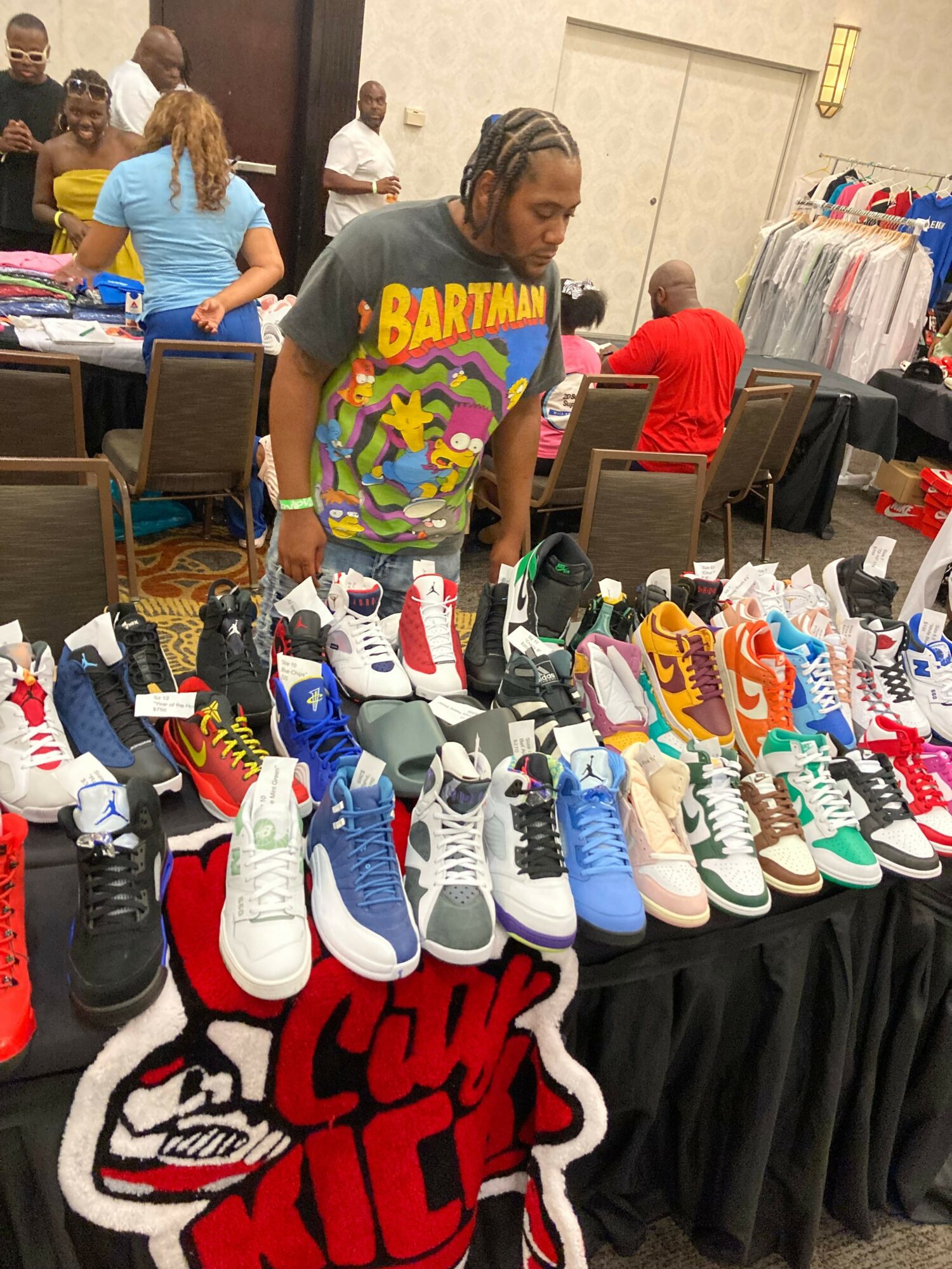 Person wearing a colorful shirt browsing a table with sports shoes and merchandise at an indoor event.