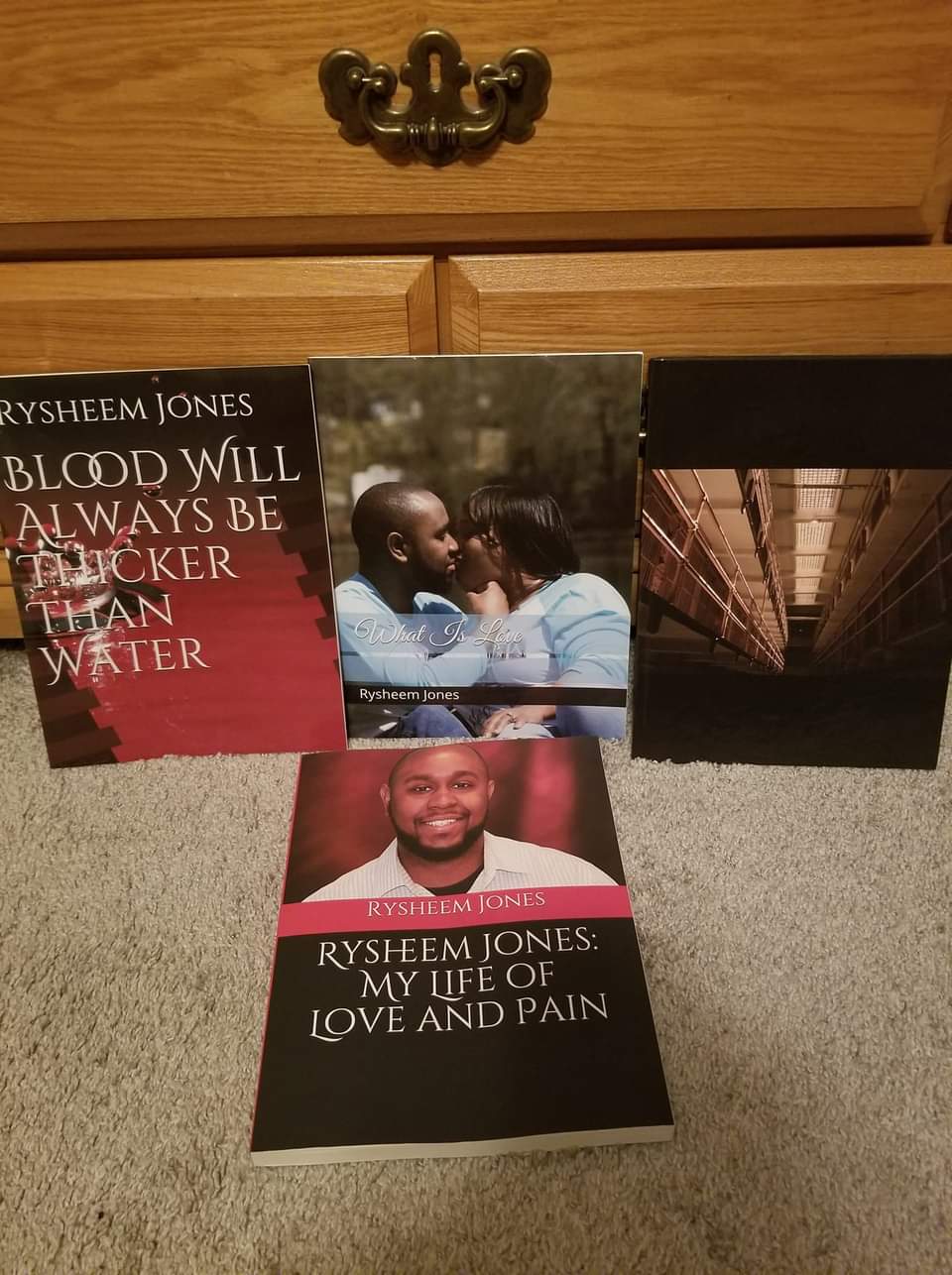 Two books and a photograph on a wooden surface, with a drawer handle above. One book titled 'Blood Will Always Be Thicker Than Water'.
