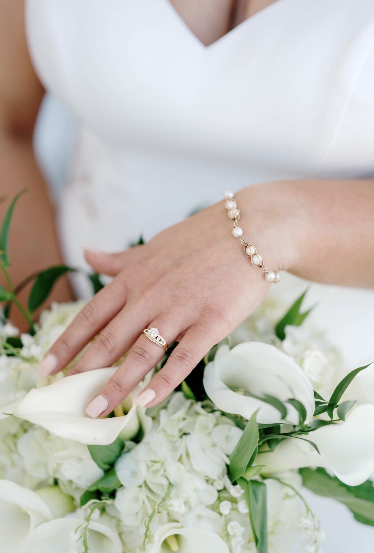 Close-up of a woman's hand with a pearl bracelet and ring, resting on a bouquet of white flowers.