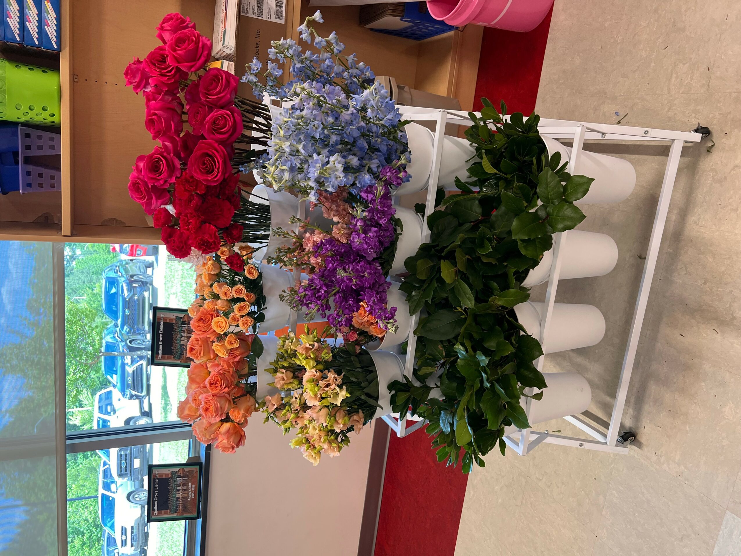 Display of colorful flowers including roses, lavender, and other blooms on a white stand in a store.