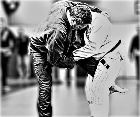Two people practicing judo, one in a gi and the other in a jacket, gripping each other's uniforms during a match.