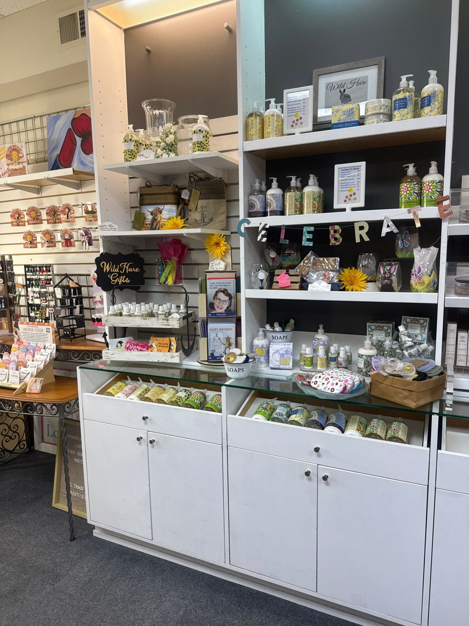 Display shelf with various decorative items, flowers, and framed pictures, arranged on shelves and a white cabinet below.