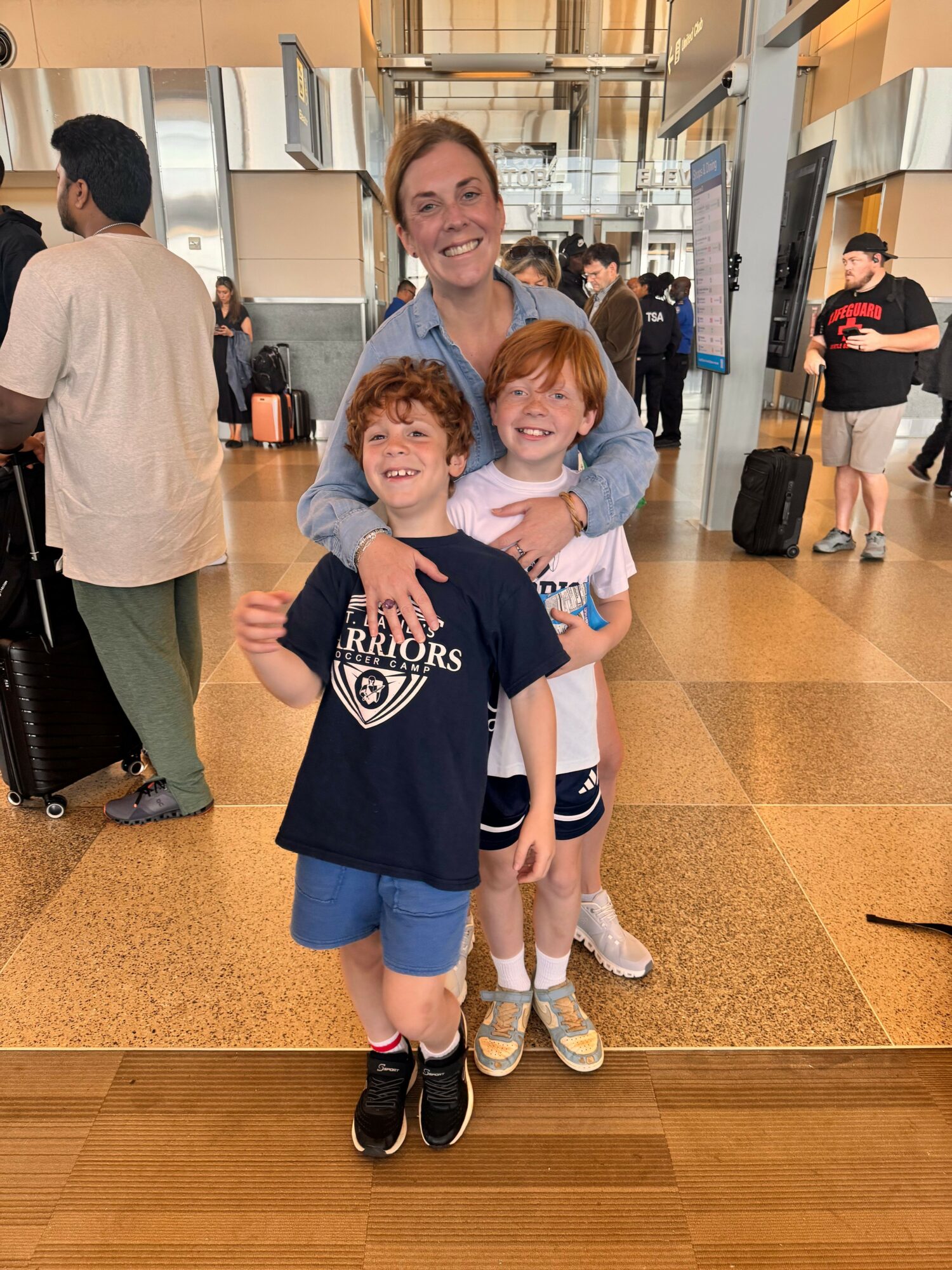 Three young women and a young girl pose together in an airport terminal, smiling and making peace signs.