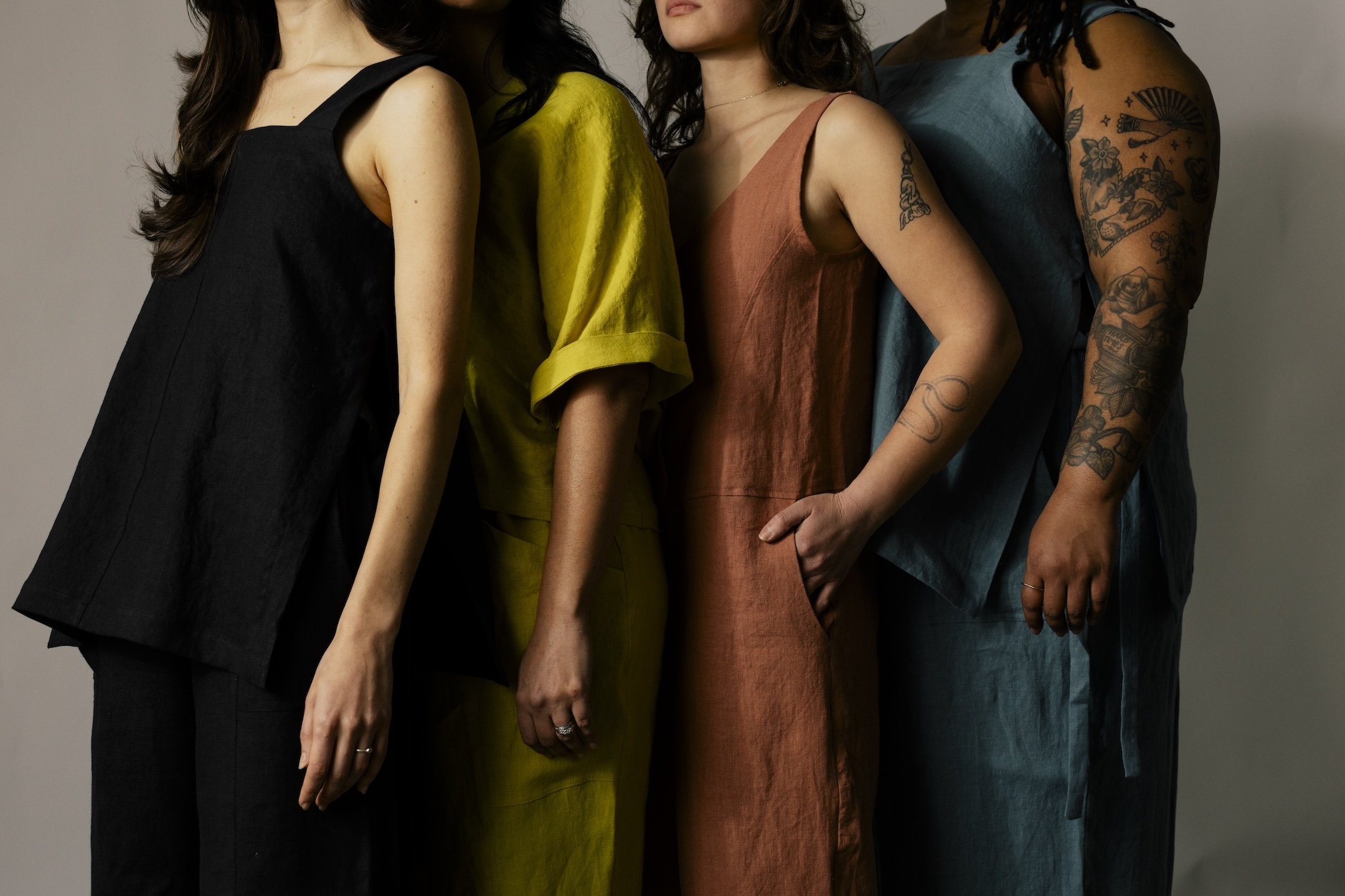 Four women standing side by side, wearing colorful dresses, with only their torsos and arms visible.