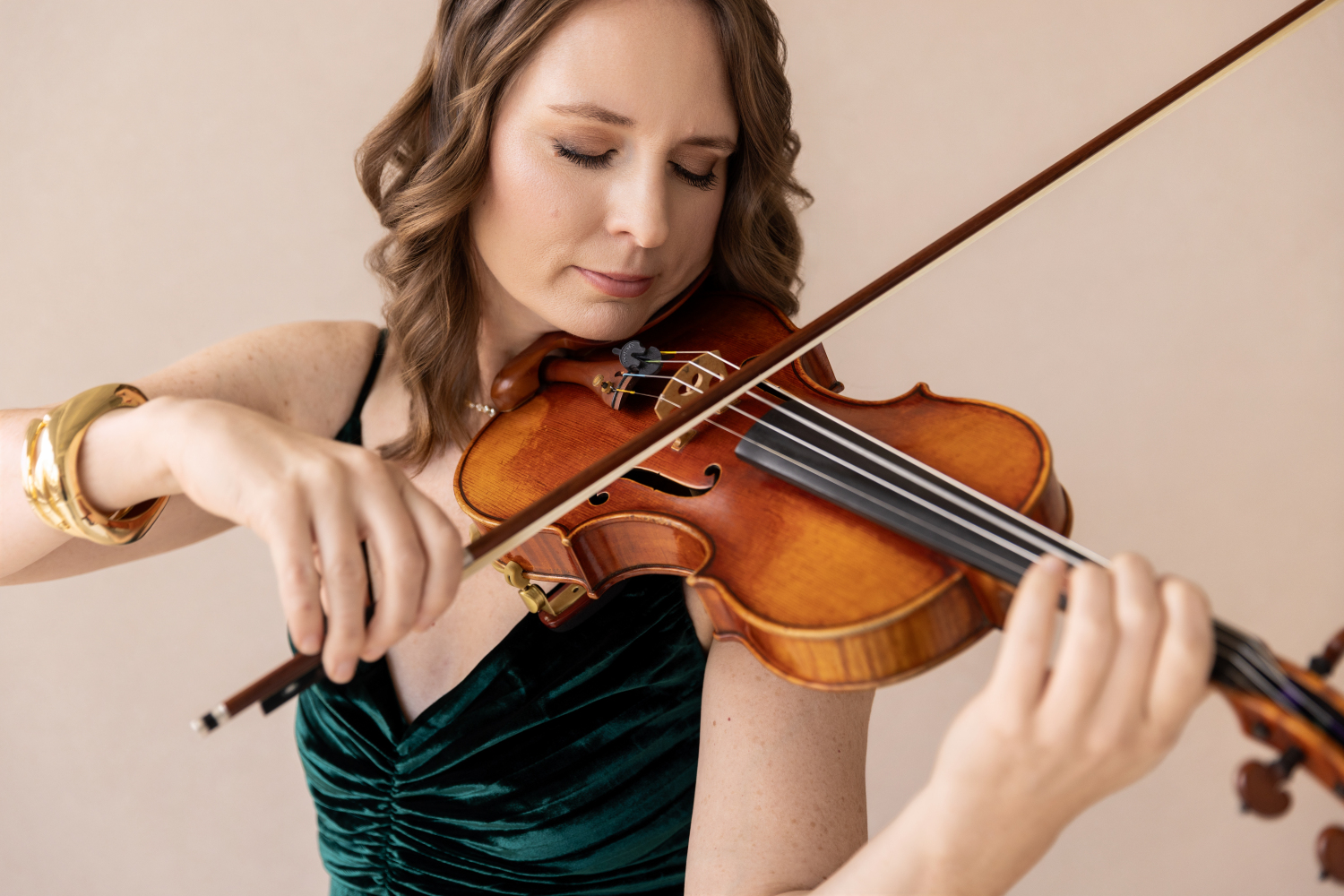 Woman playing a violin, focusing on her instrument and hand positioning, with a neutral background.