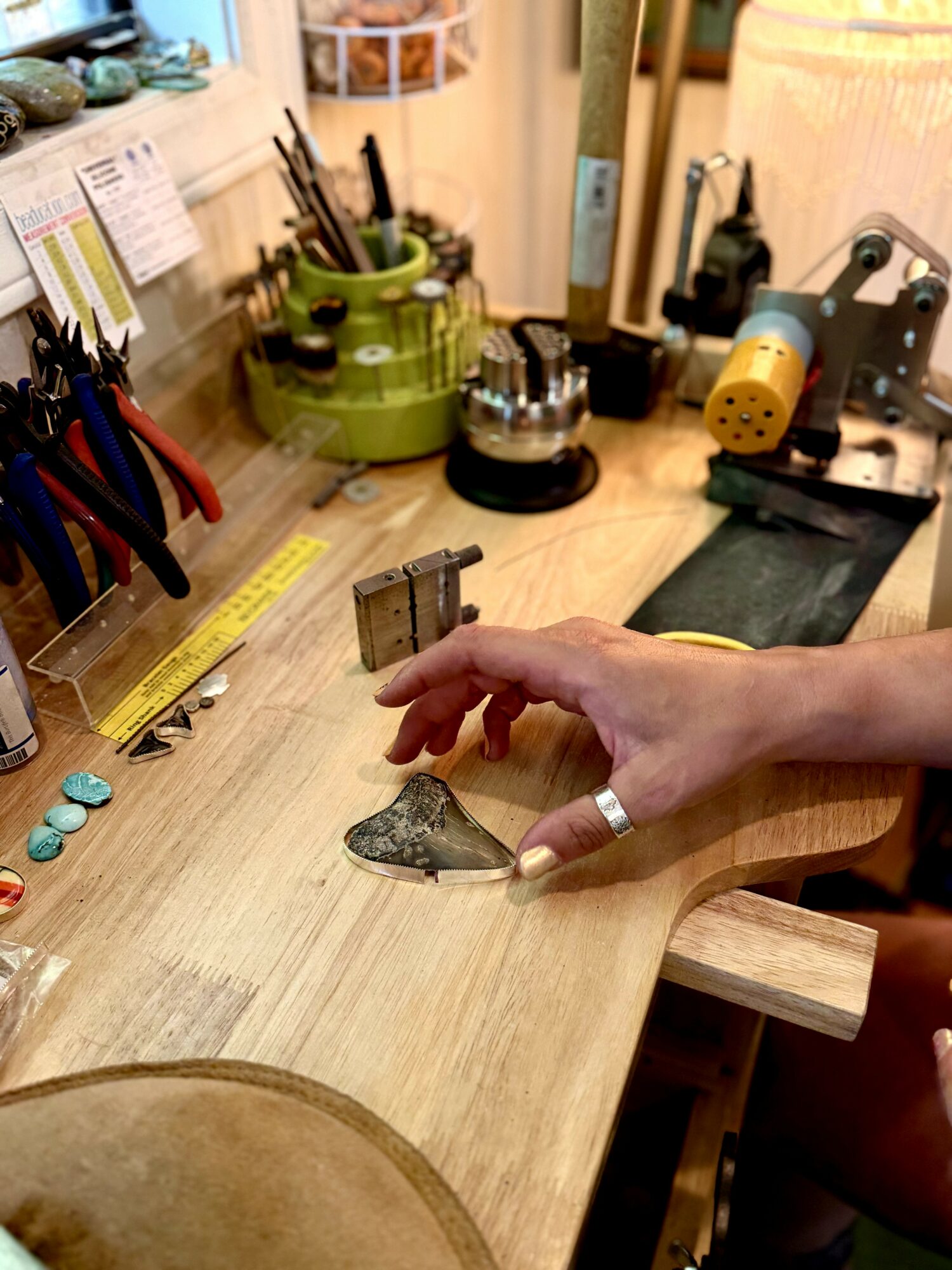 Hand holding a small metal object on a wooden workbench with tools and equipment in the background.
