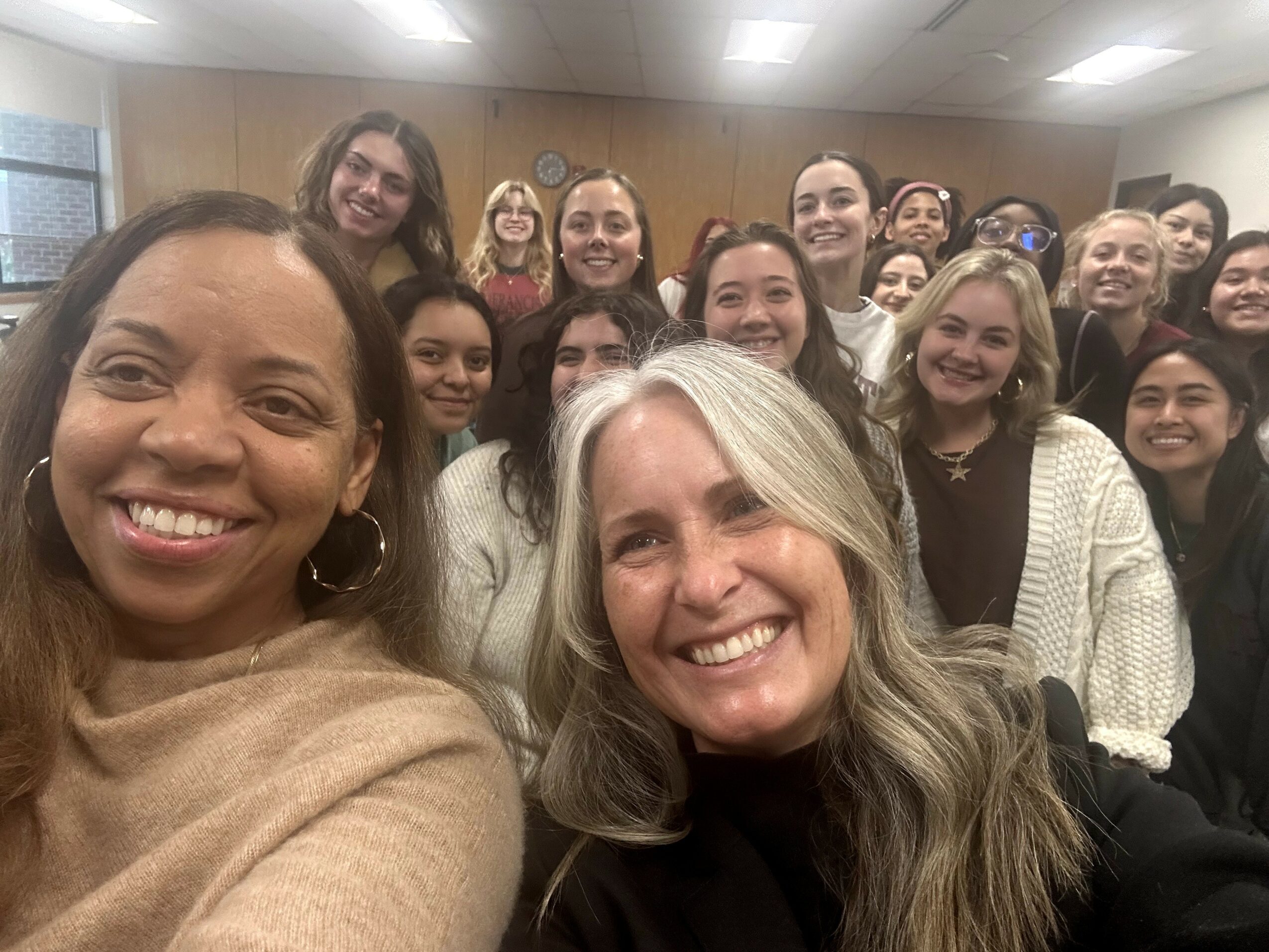 Group of smiling women in a room, taking a selfie together.