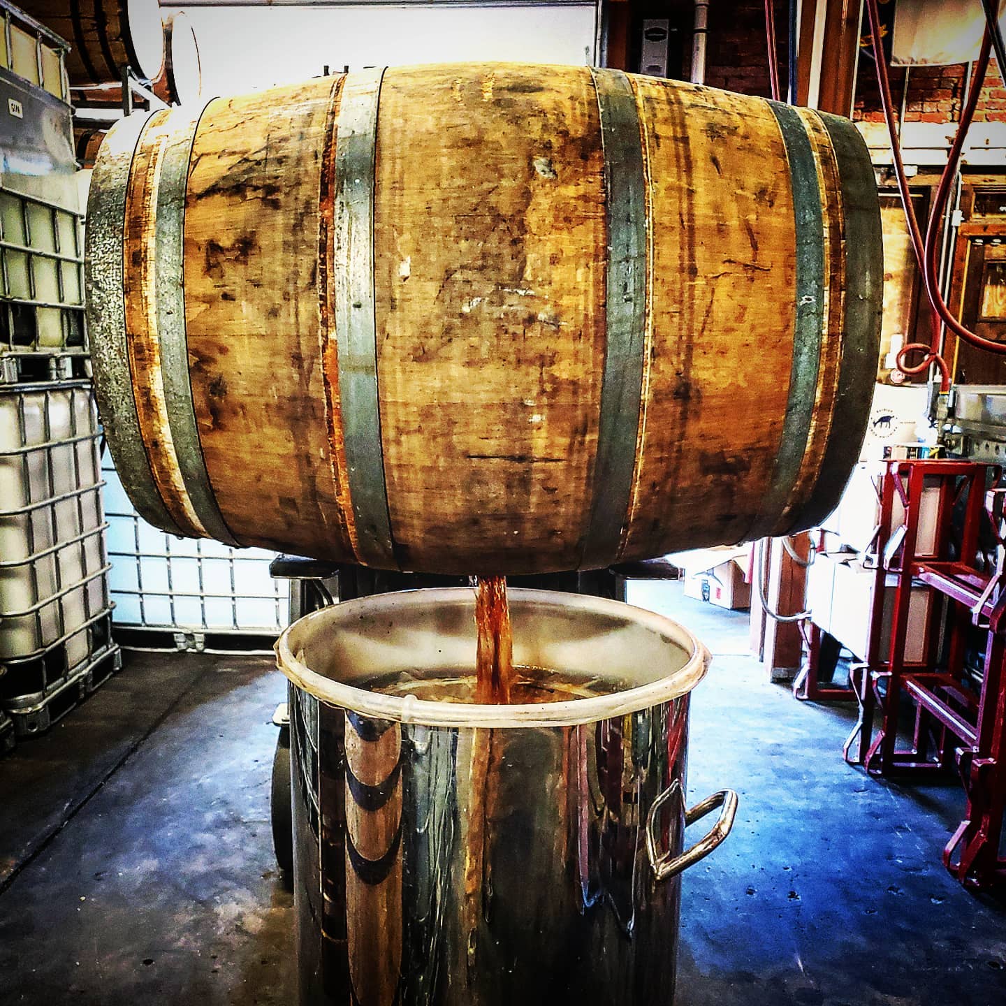 Large wooden barrel above a shiny metal container with a spout, in a workshop setting.
