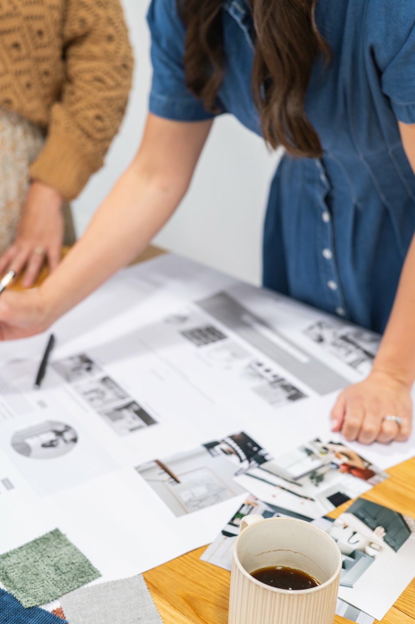 Person in blue shirt working on architectural plans, with a coffee mug and photos on table.
