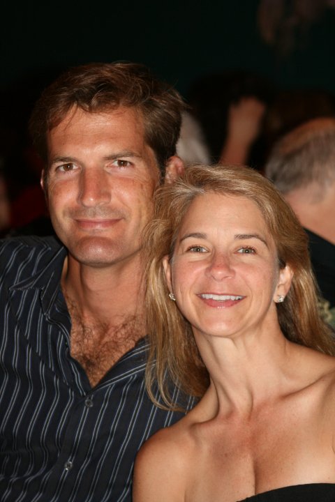 A man and woman smiling closely together in a dimly lit setting.
