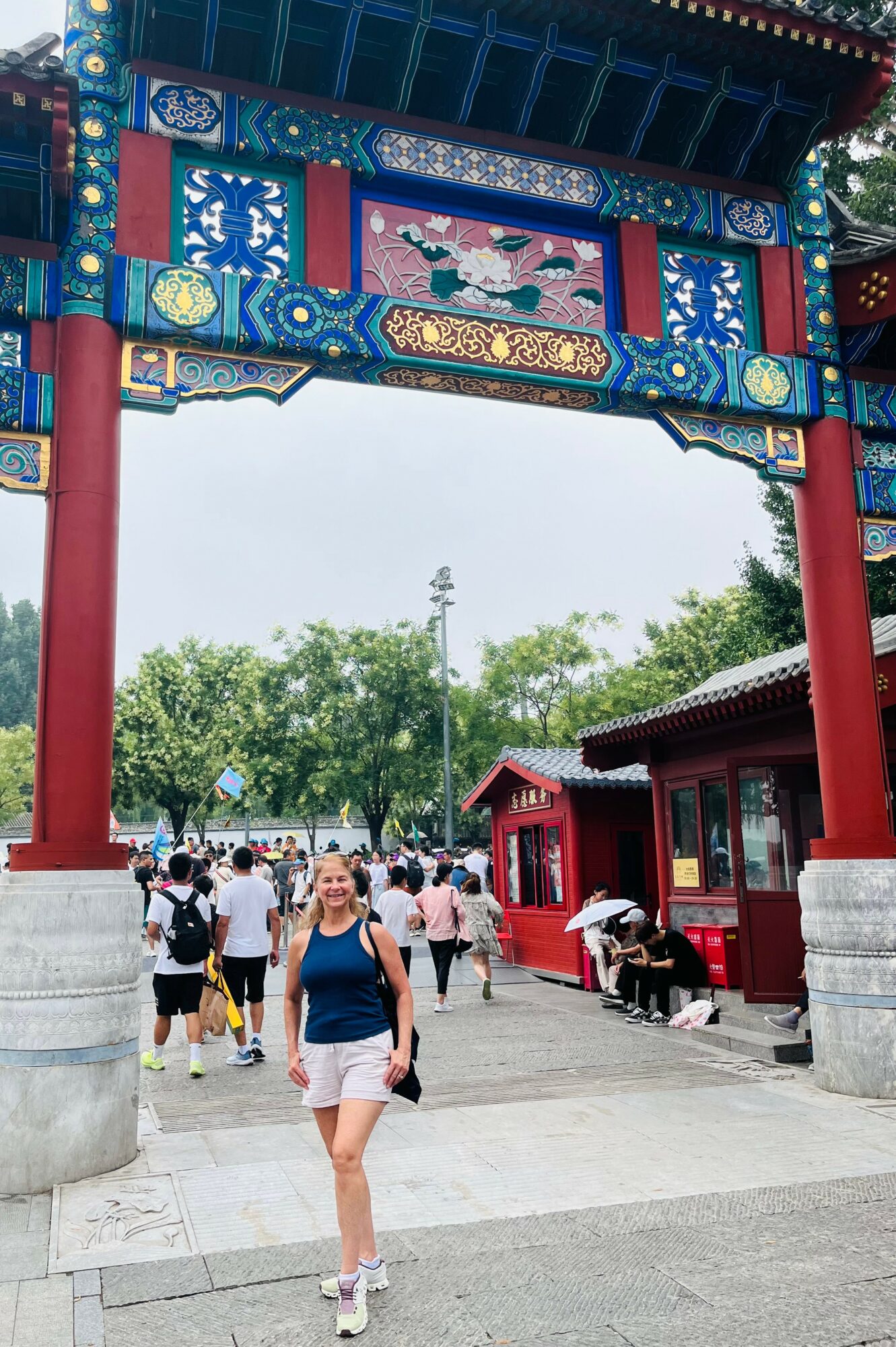 People walking under a colorful traditional Chinese gate with trees in the background.