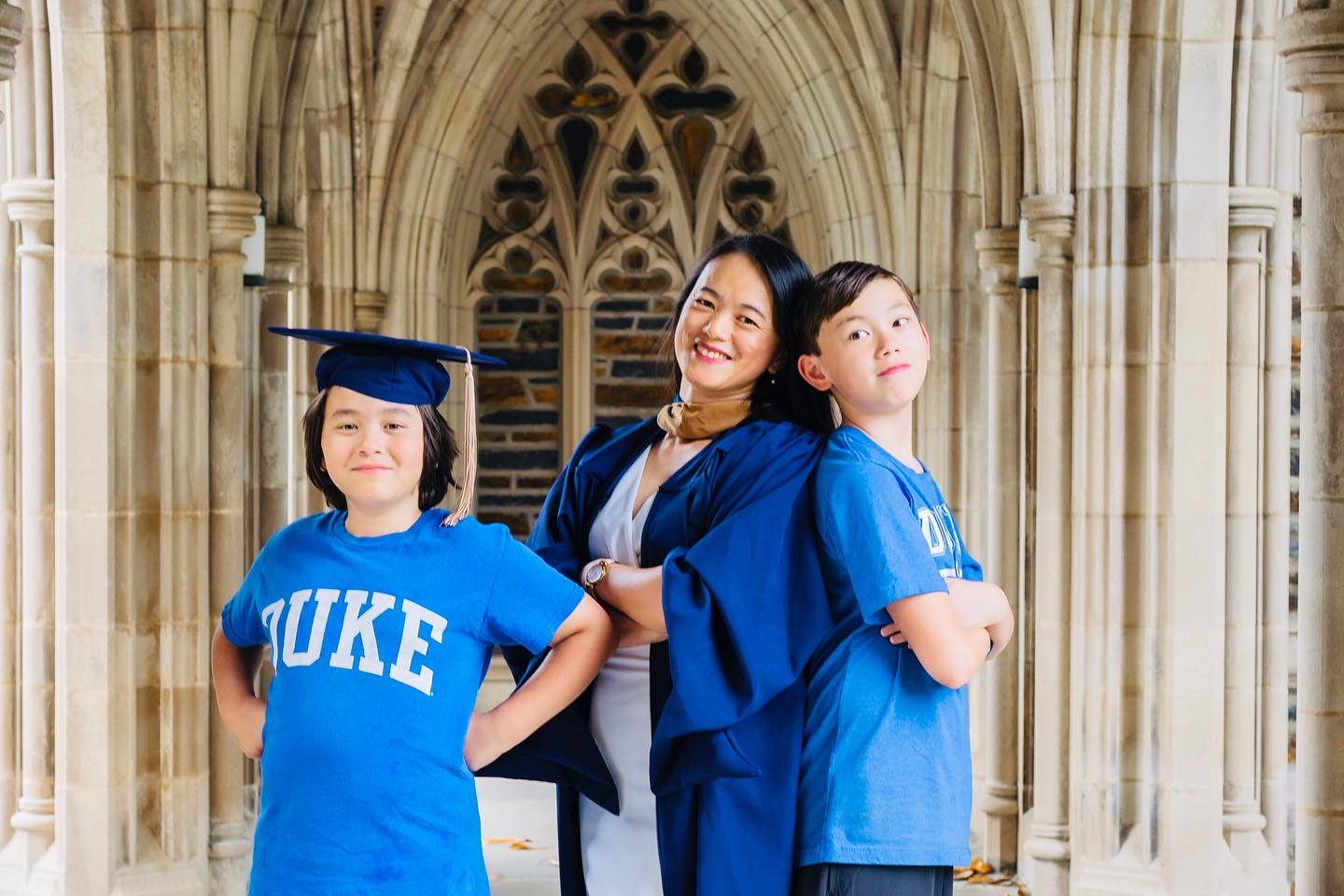 Three people in blue graduation gowns and caps standing in front of a cathedral, smiling and posing.