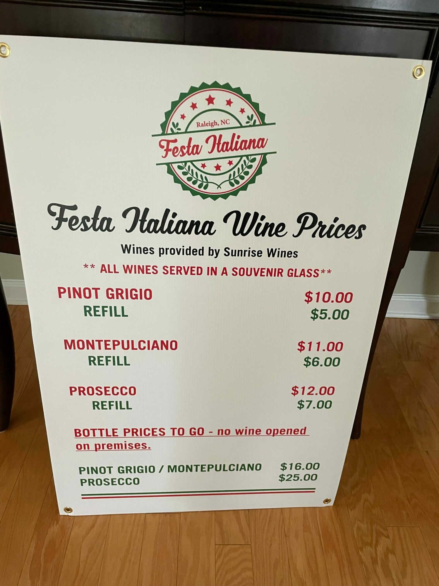 Menu board listing prices for various wines and food items at Festas Italianas, with a white background and red and green text.