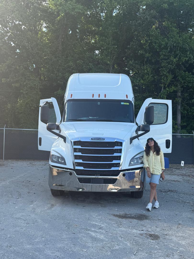 Person standing next to a large white truck with open doors, outdoors with trees in the background.