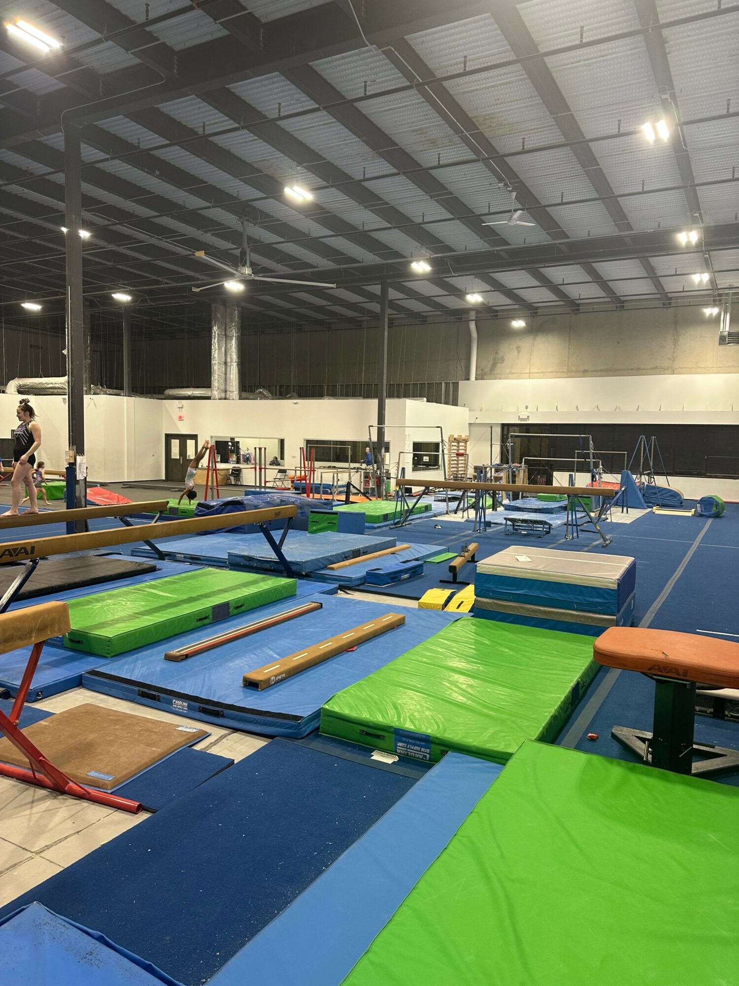 Indoor gym with colorful mats, equipment, and high ceiling with lights, viewed from a tilted angle.