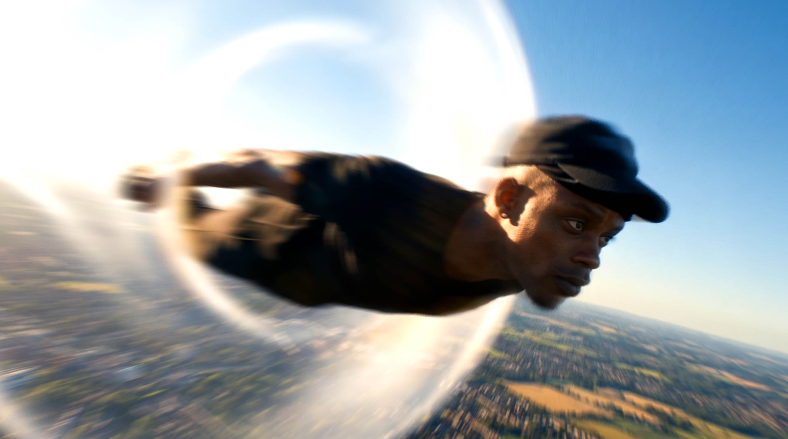 Person skydiving with a landscape below, head facing forward, sky and clouds in background.