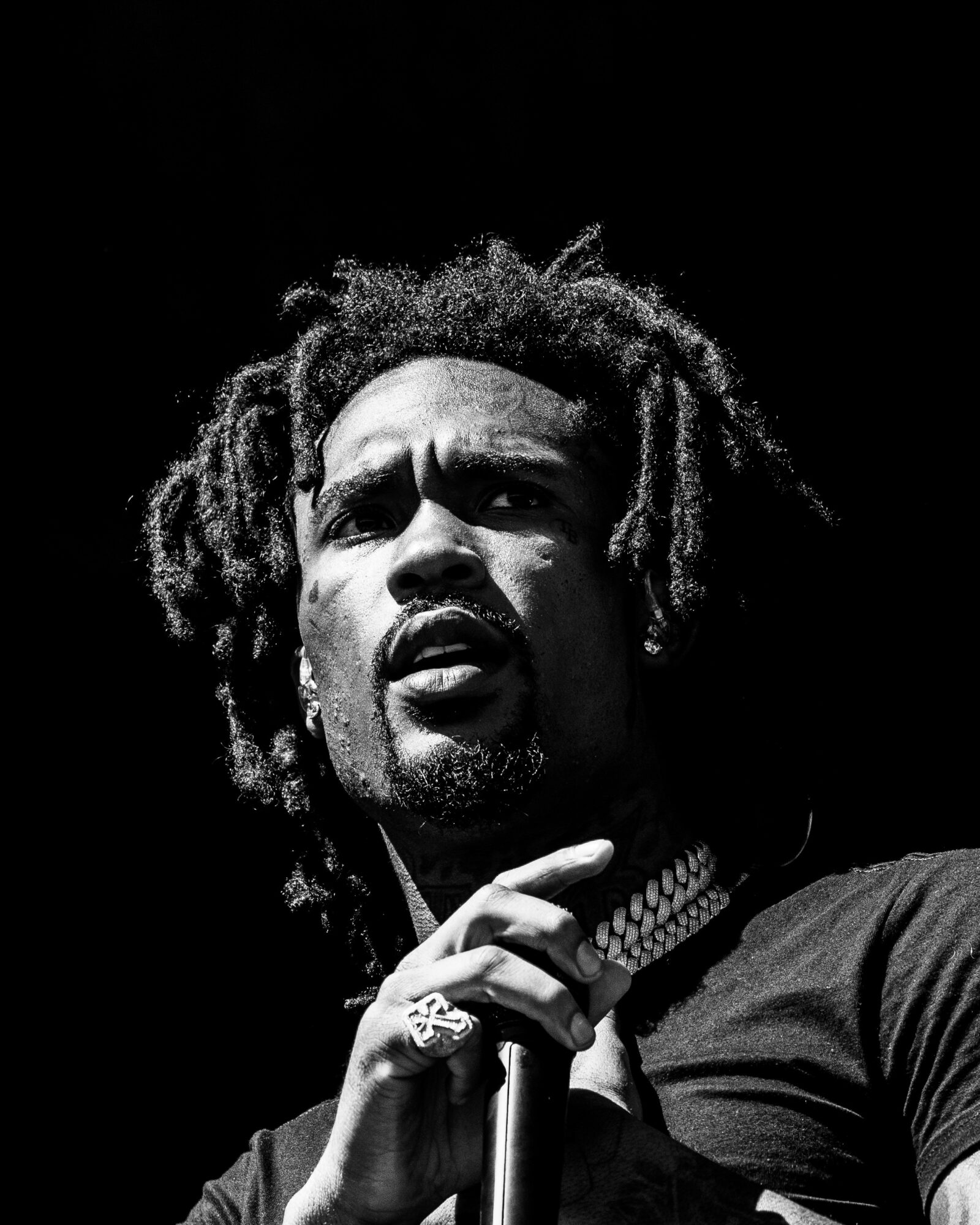 Man with dreadlocks holding a microphone, looking serious, in black and white.