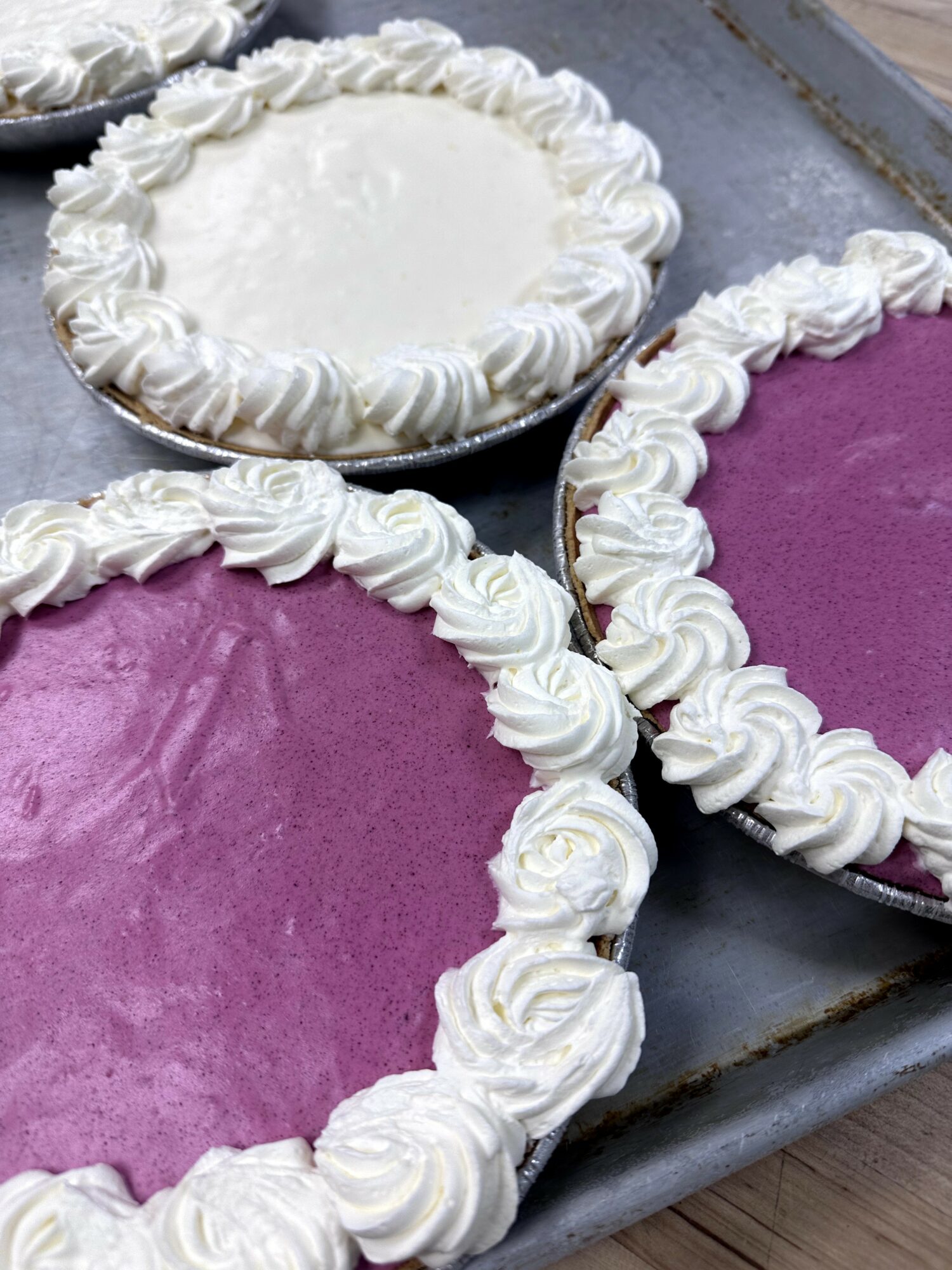 Three heart-shaped cakes with white and purple frosting, decorated with piped rosettes, on a metal tray.