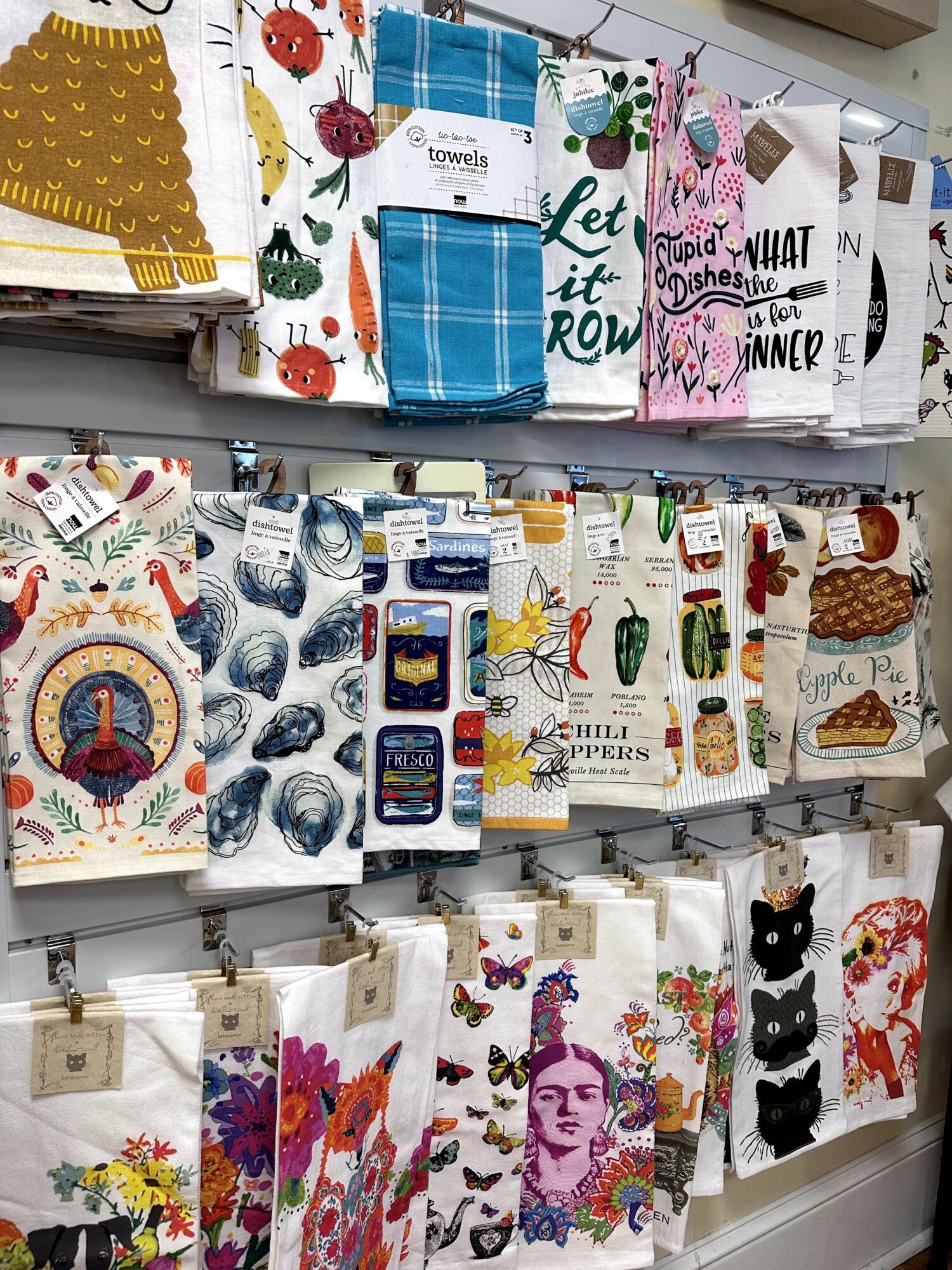 Display of colorful kitchen towels with various patterns and designs hanging on a wall.