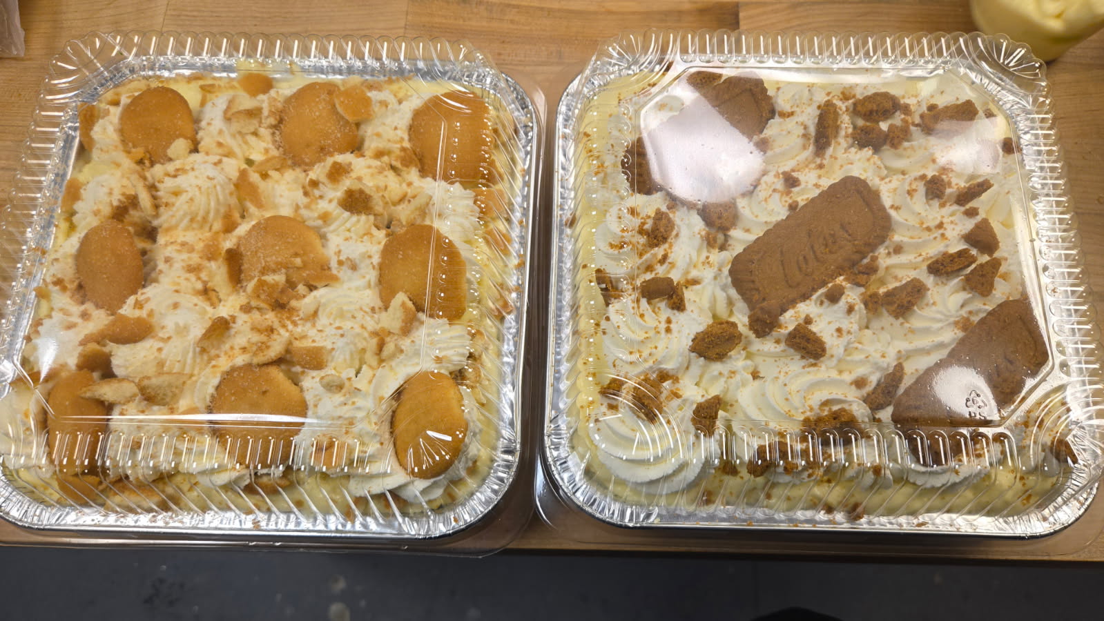 Two aluminum trays with desserts, one with cookies and the other with ice cream and toppings, on a wooden surface.