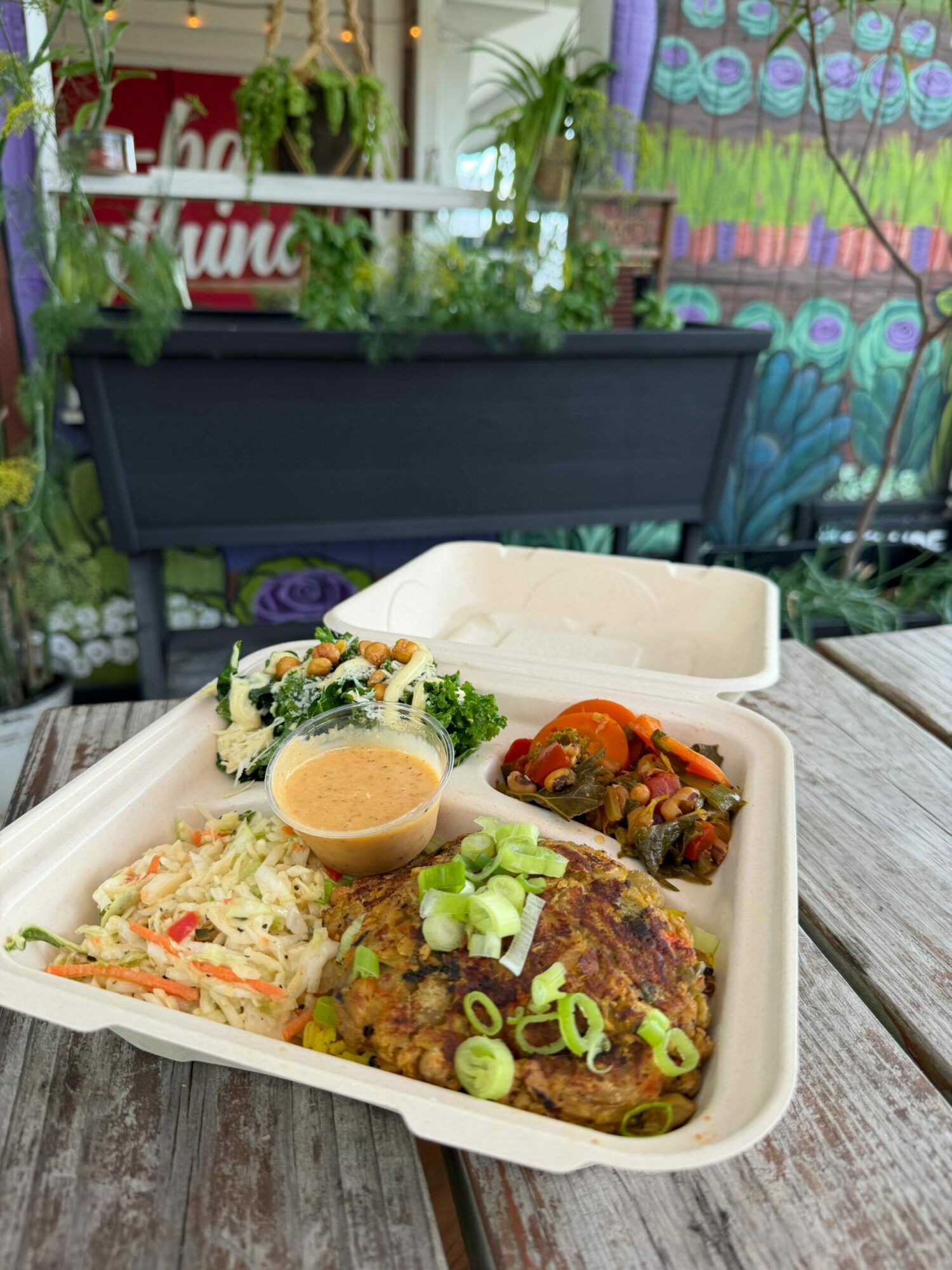 Tray with a burger, coleslaw, and a side of vegetables on a wooden table.