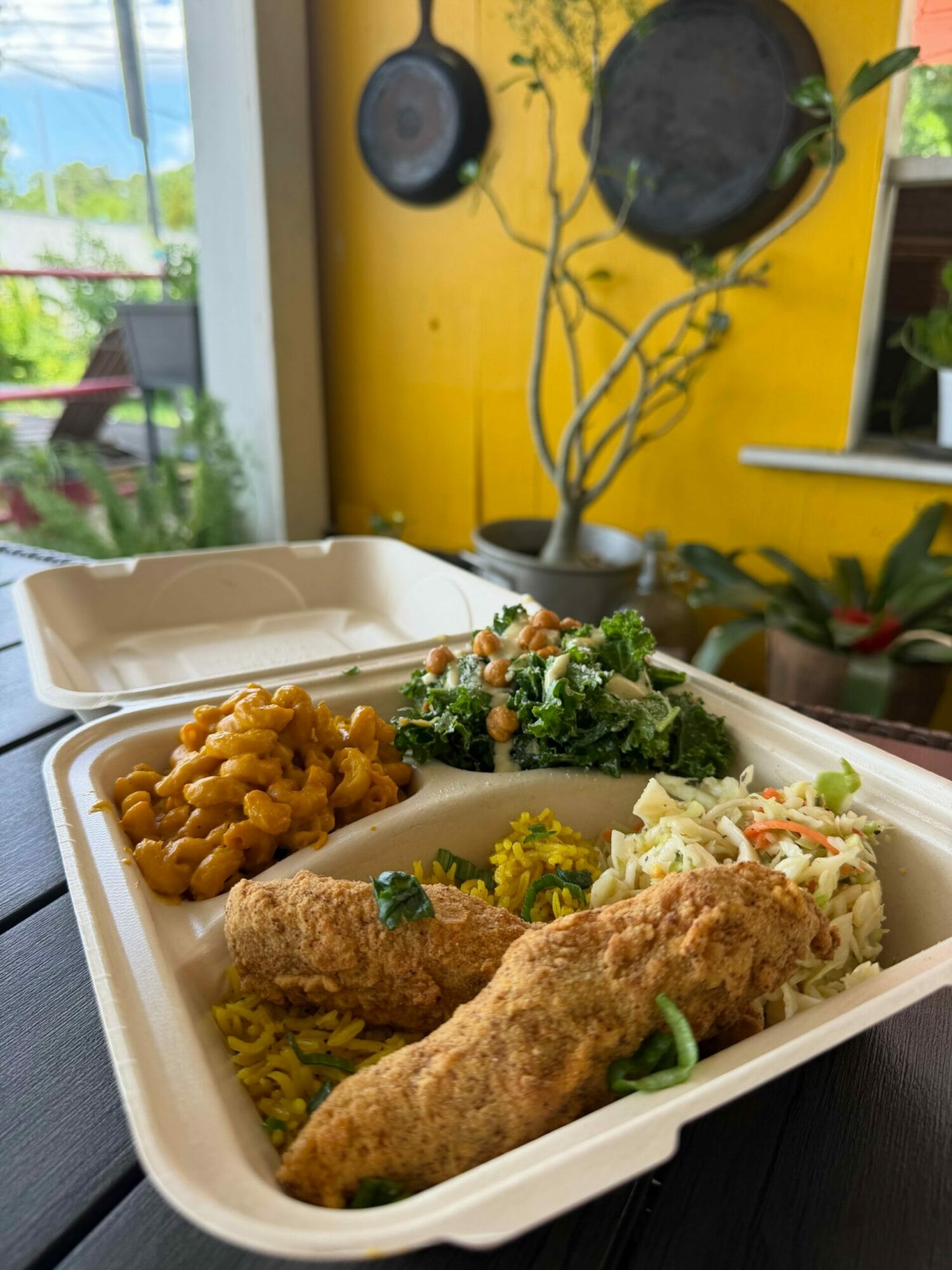 Food in a takeout container with rice, vegetables, and a wrap, on a dark surface.