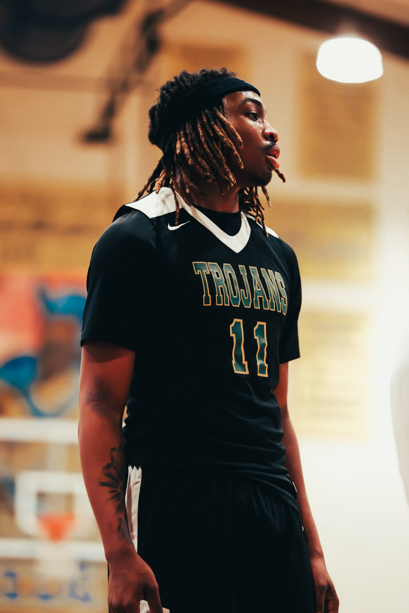 Young male basketball player in black jersey with number 11, standing indoors, side profile, focused expression.