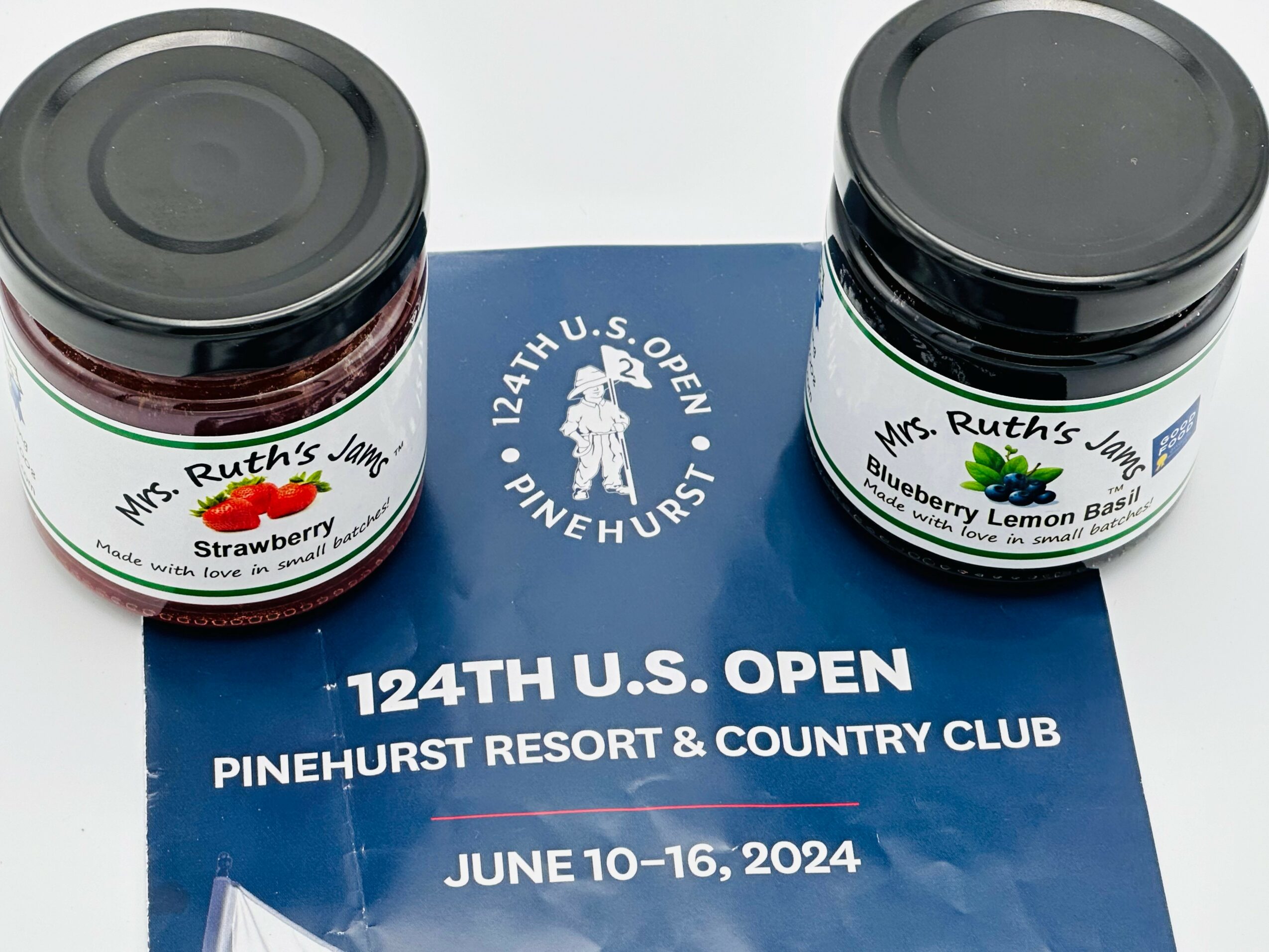Two jars of jam on a table with a blue and white sign for the 124th U.S. Open, June 10-16, 2024.