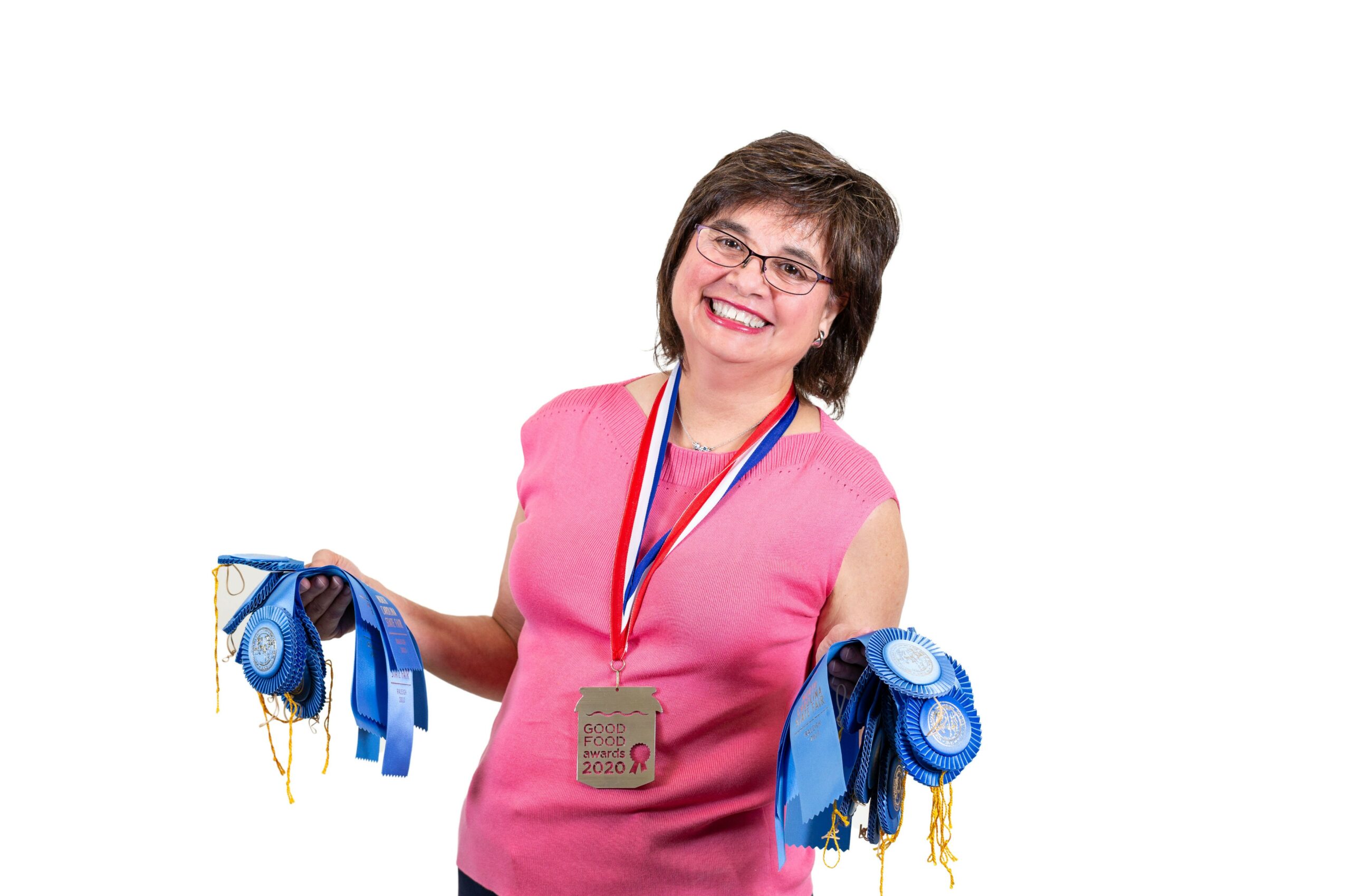 Smiling woman wearing a pink top and medals, holding blue ribbons, against a white background.