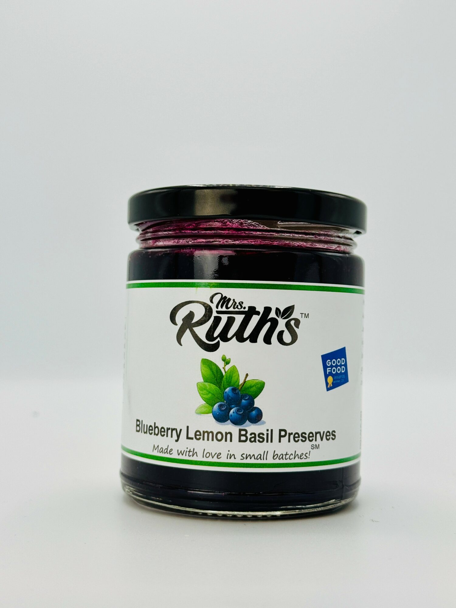 Jar of blueberry lemon basil preserves with a black lid and label showing blueberries and basil leaves, on a white background.
