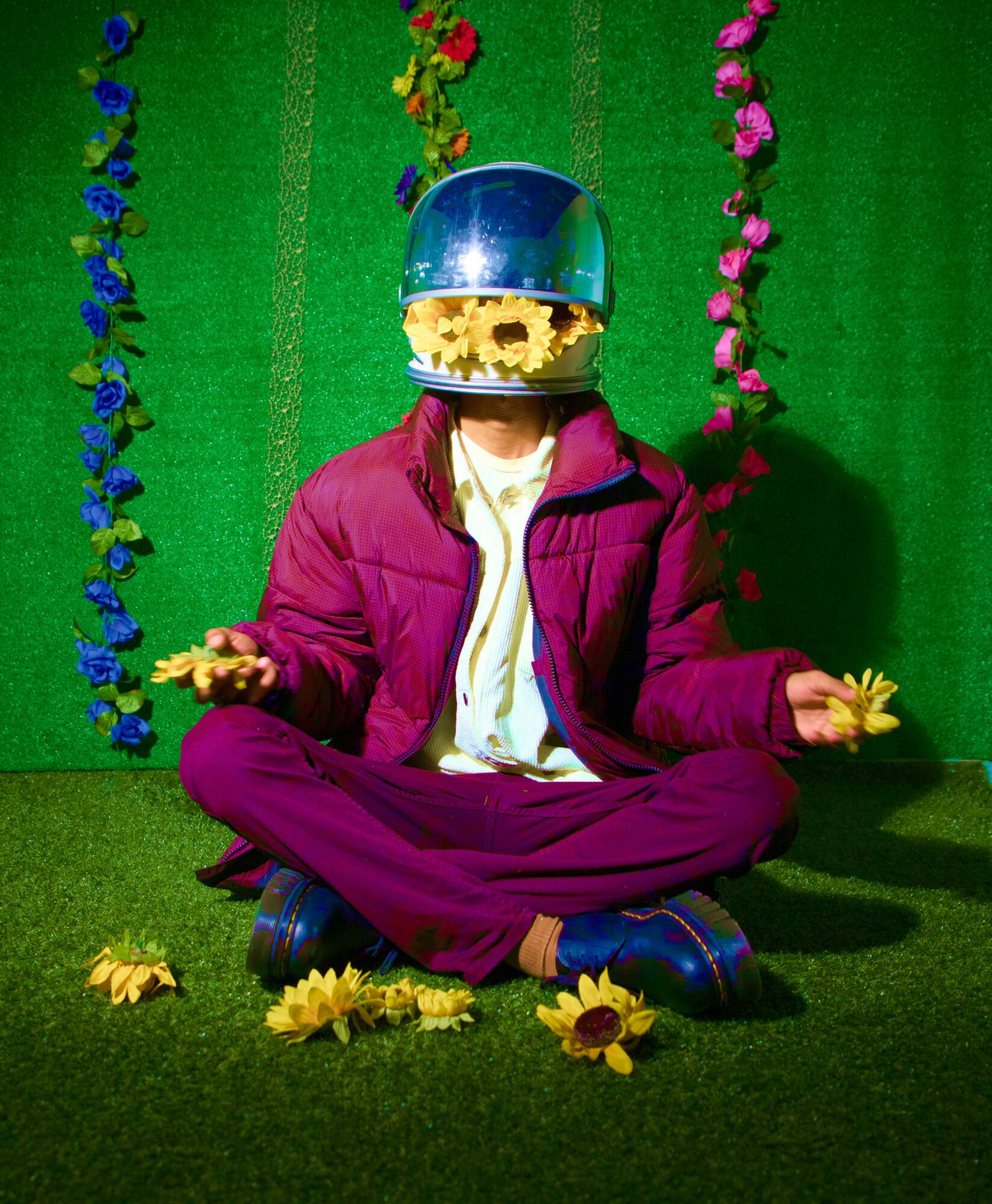 Person sitting cross-legged with a reflective helmet, surrounded by colorful flowers and green background.