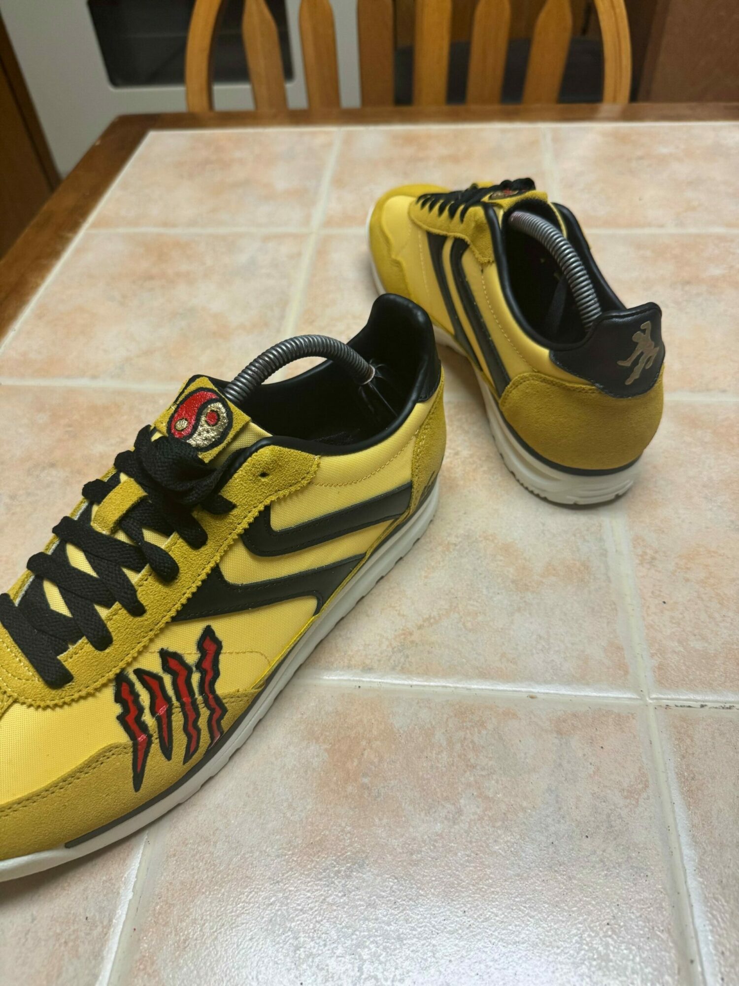 Pair of yellow and black sneakers on tiled floor, one shoe upright and the other tilted sideways.