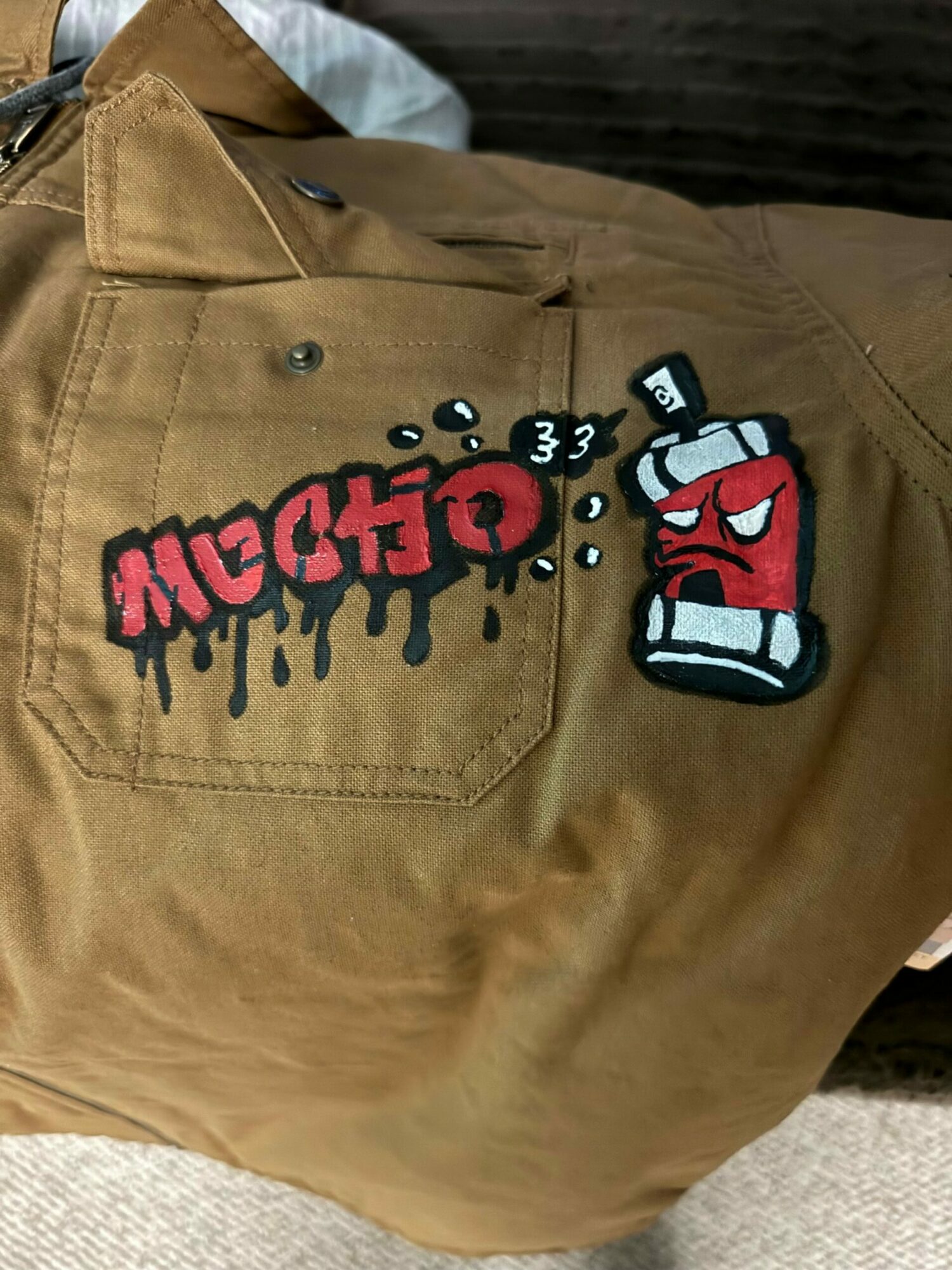 Brown jacket with a patch of a red and white glove and the word 'MACHINE' embroidered below.