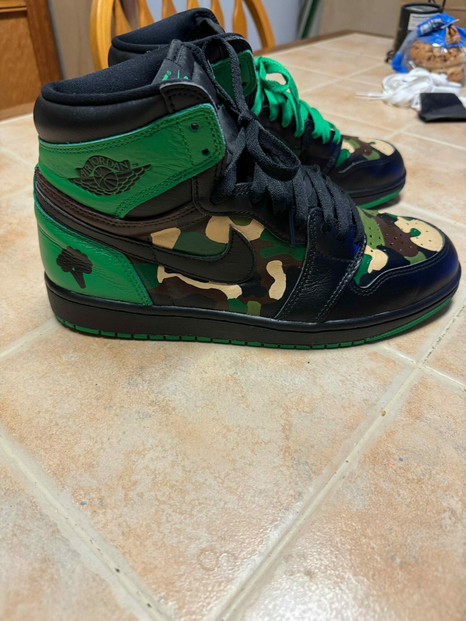 Pair of camouflage and green sneakers on tiled floor, with laces tied and tongue visible.