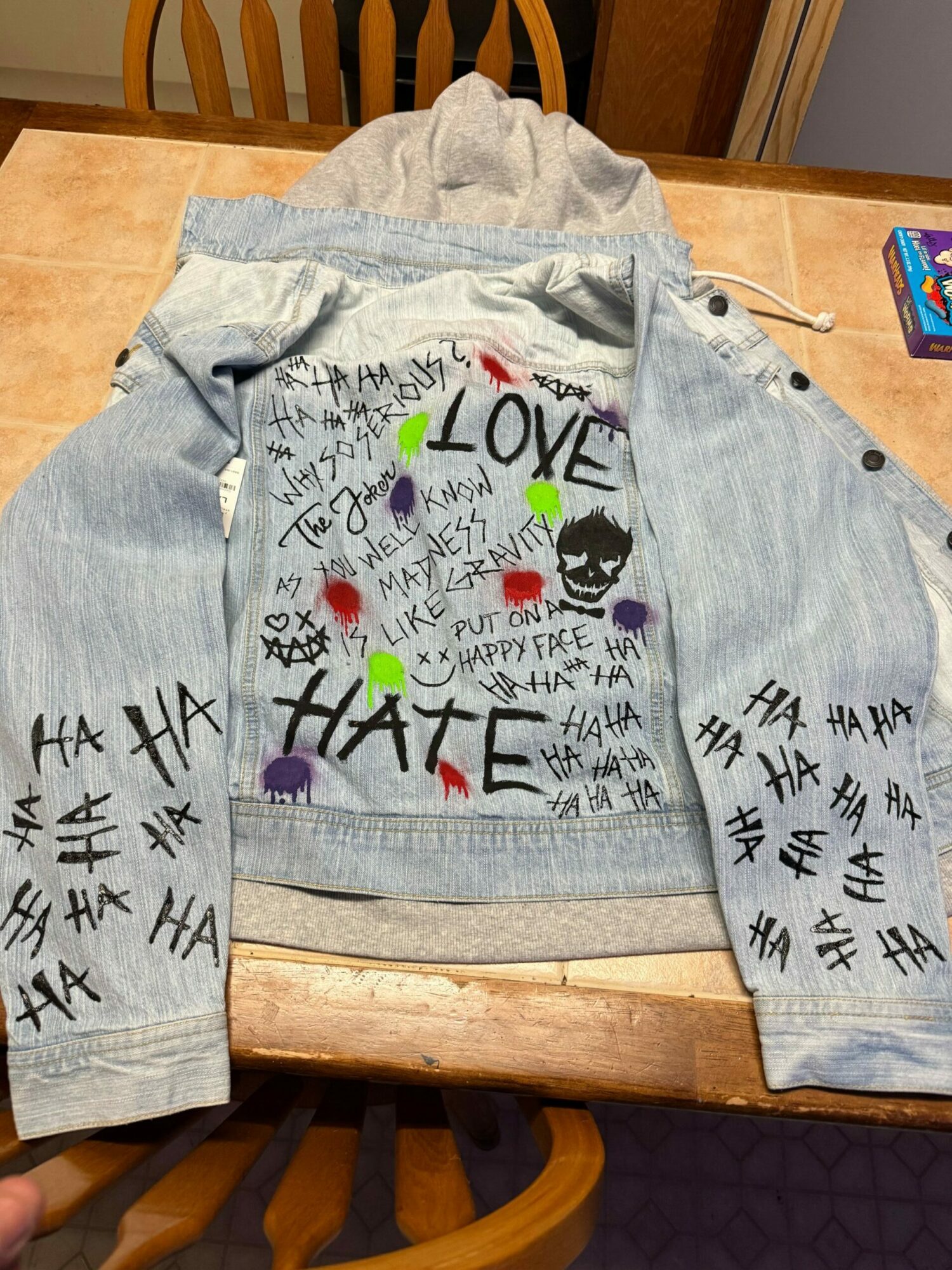 Gray hoodie with colorful and black text, hearts, and symbols, laid flat on a wooden table.