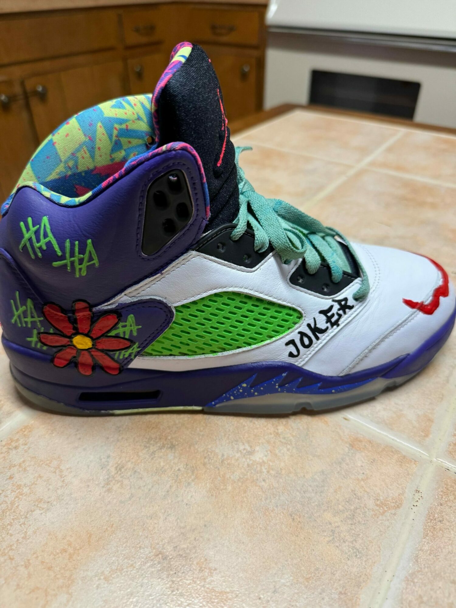 Sneaker with colorful design, green and purple accents, and a red flower on the side, on a tiled floor.