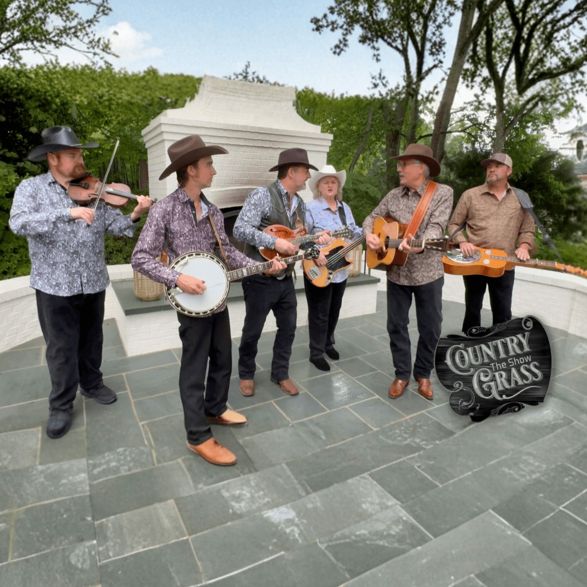Group of six musicians playing instruments outdoors near a monument, with trees and a cloudy sky in the background.
