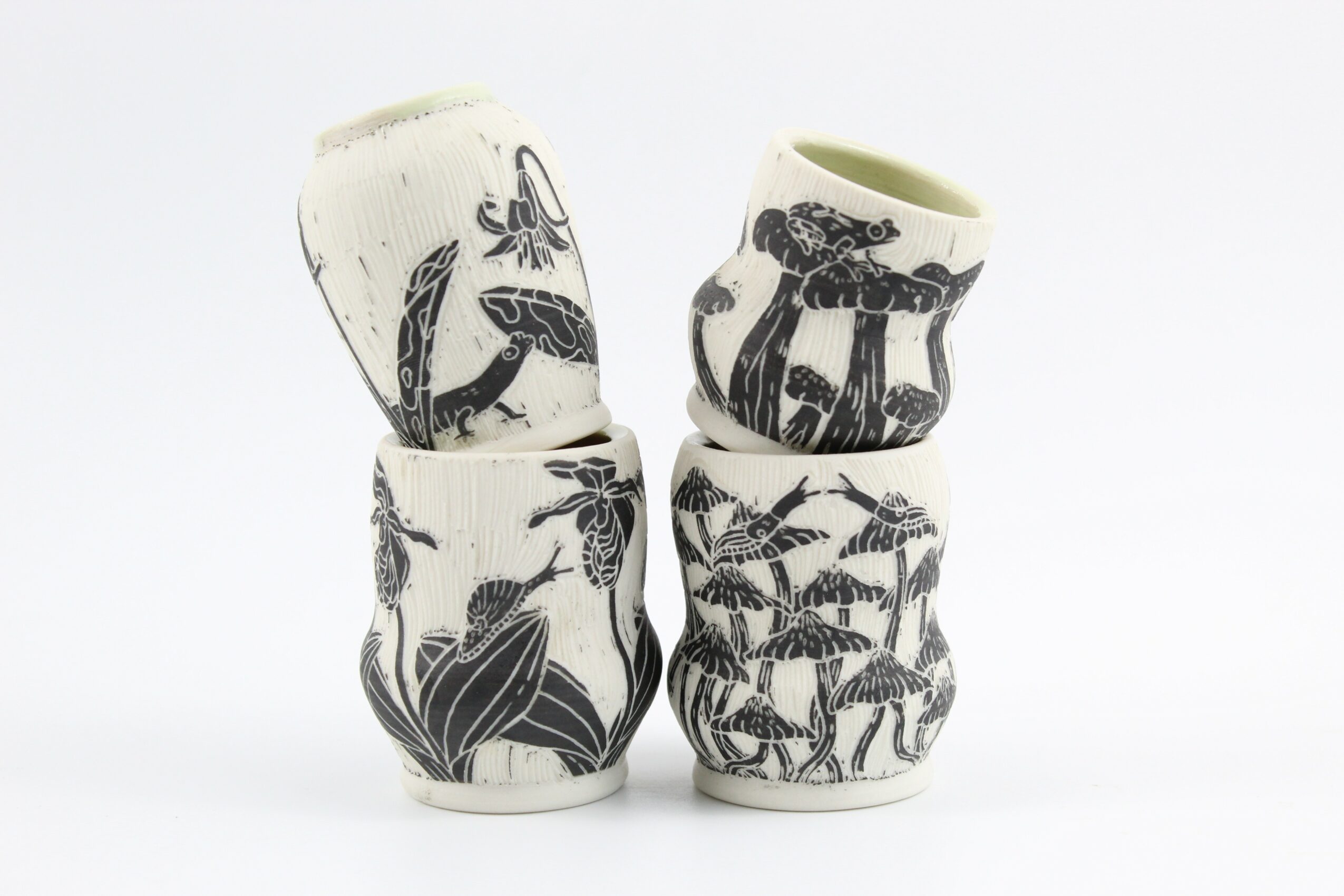 Four ceramic cups with black animal and plant illustrations stacked against a white background.