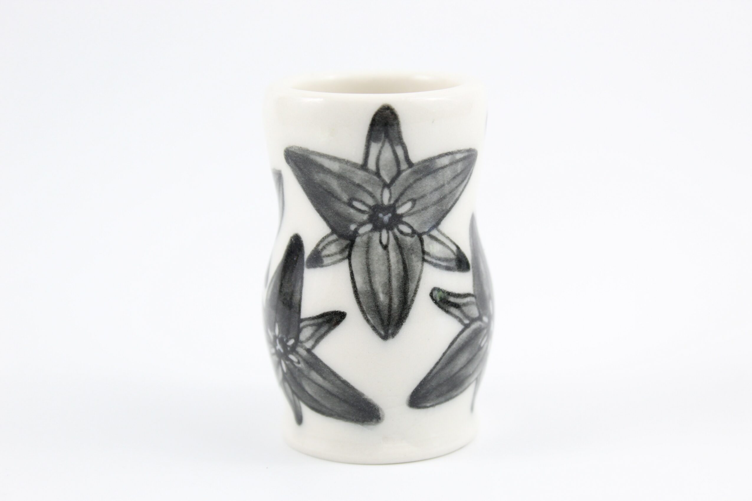 White ceramic vase with black floral design, featuring a large flower with five petals, on a plain white background.